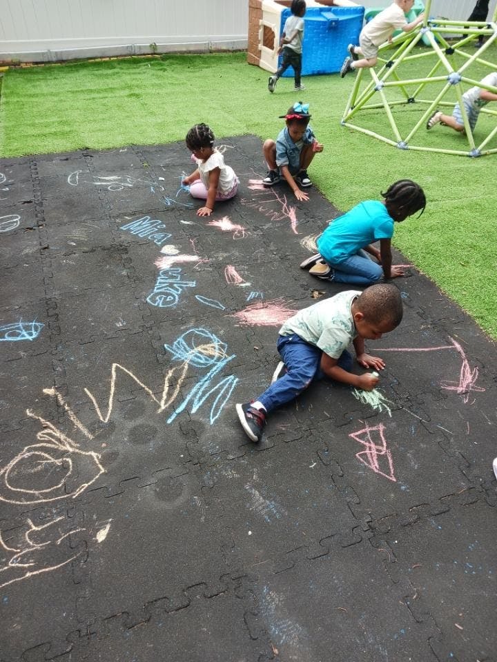 Children drawing with colorful chalk on a foam playground mat