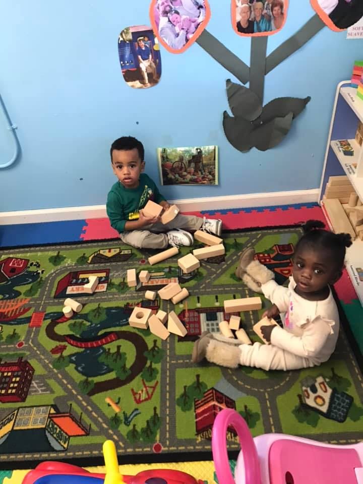 Two children playing with wooden blocks on a rug with a road map design