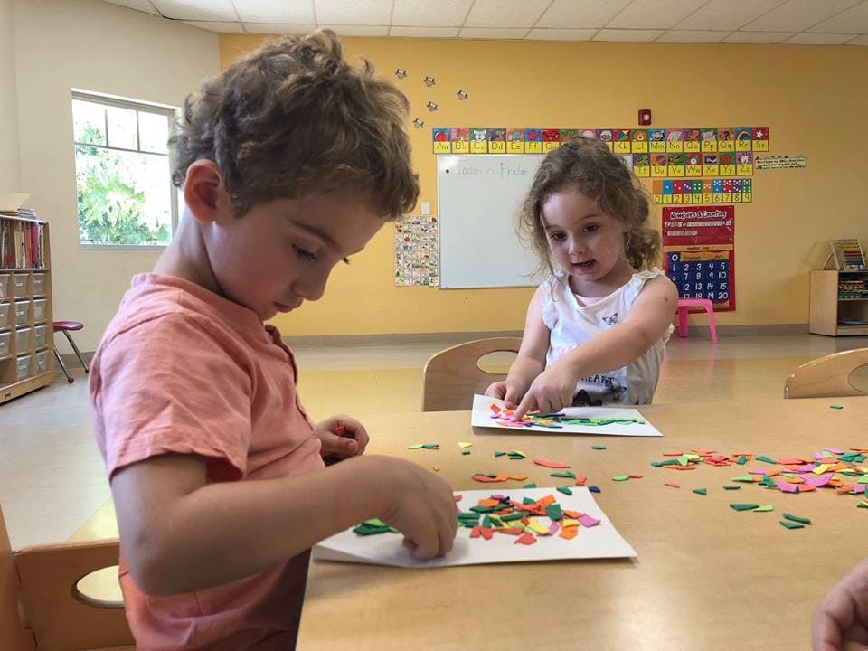 Two children doing crafts at a table in a classroom