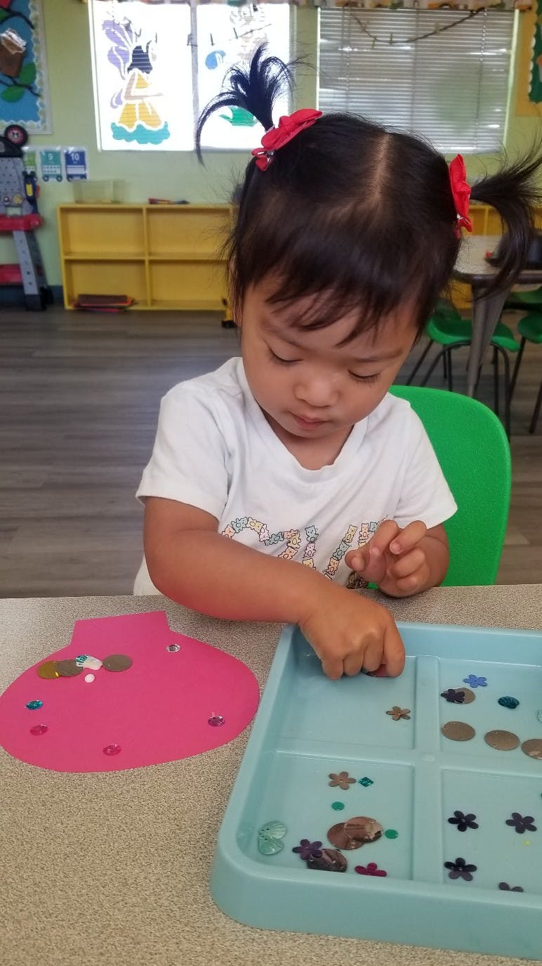 Child playing with small objects and a pink cutout at a table