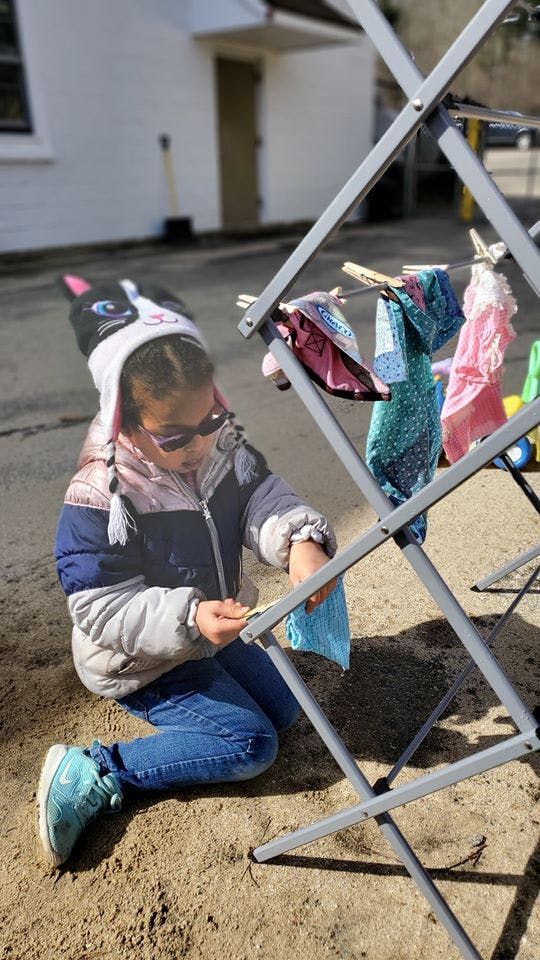 Child kneeling on ground, hanging clothes on a drying rack