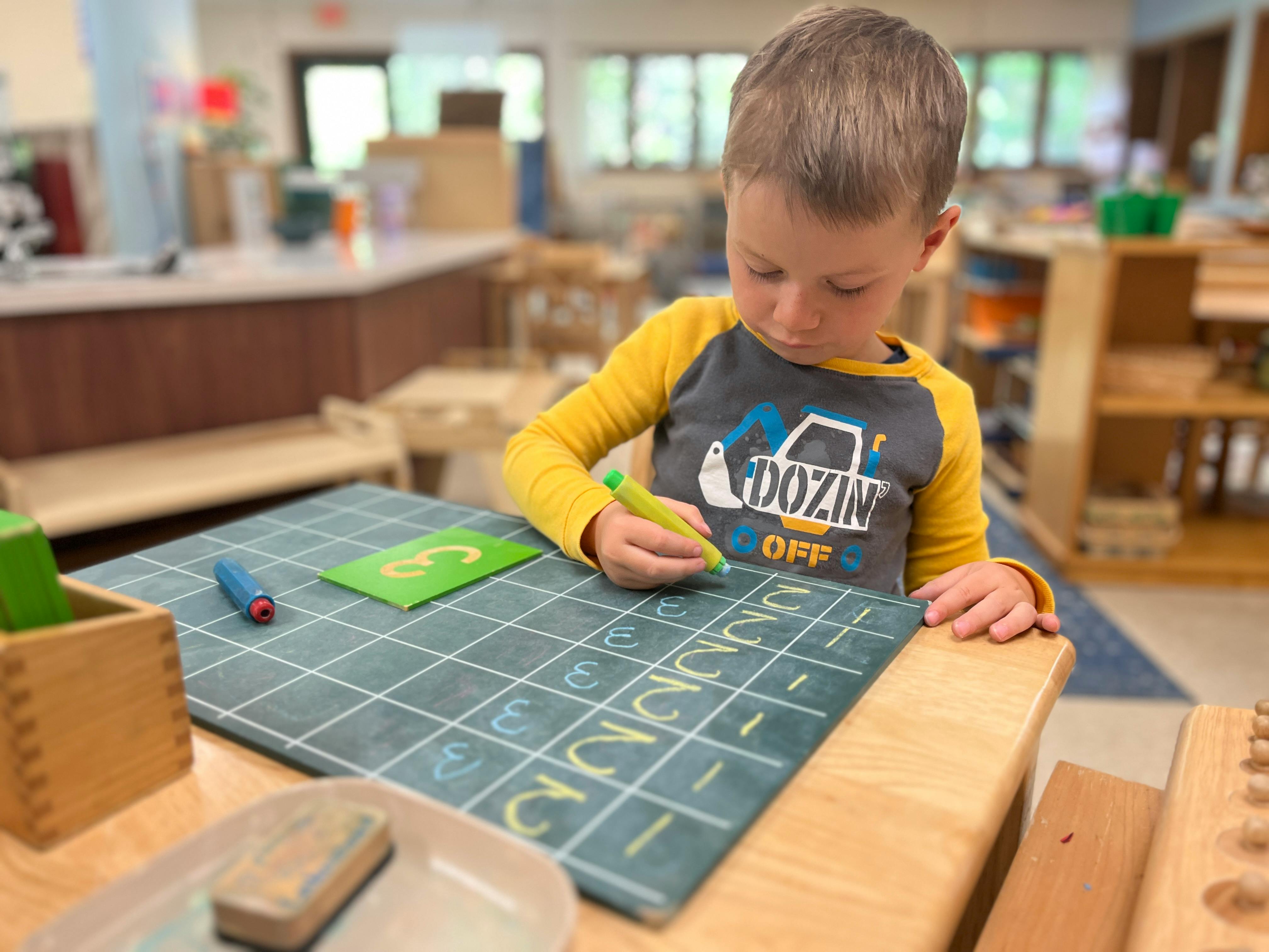 Child writing numbers on a grid with a yellow marker