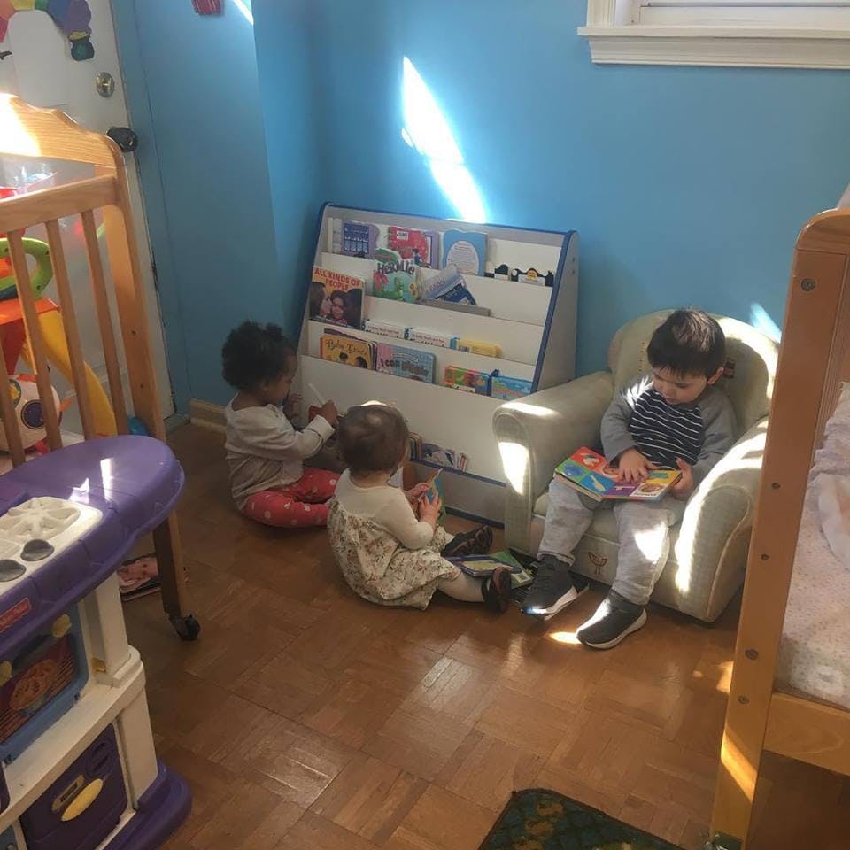 Three children in a room, one reading in a chair, two on the floor