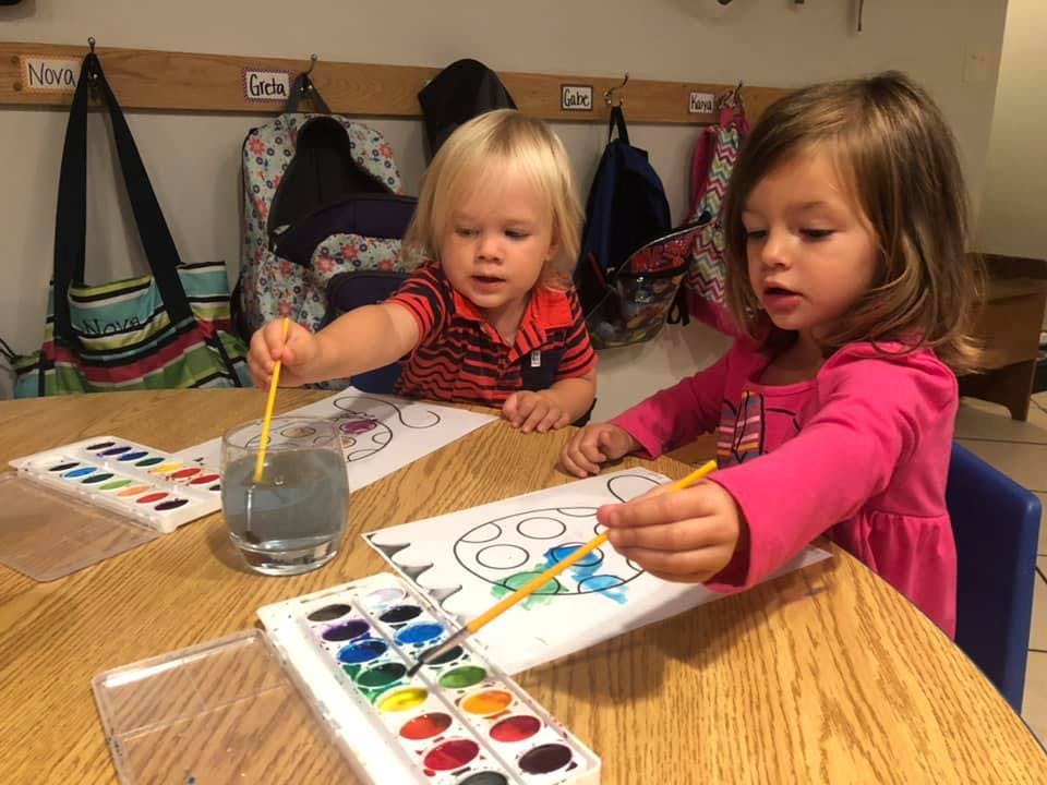 Two children painting with watercolors at a table