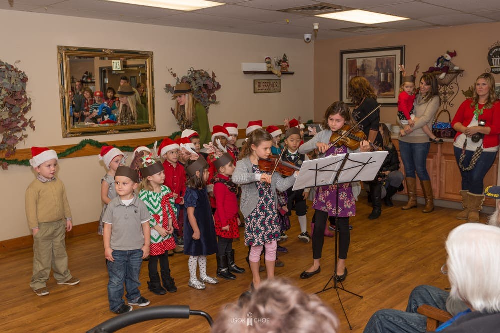 Children in Santa hats watching a child play the violin