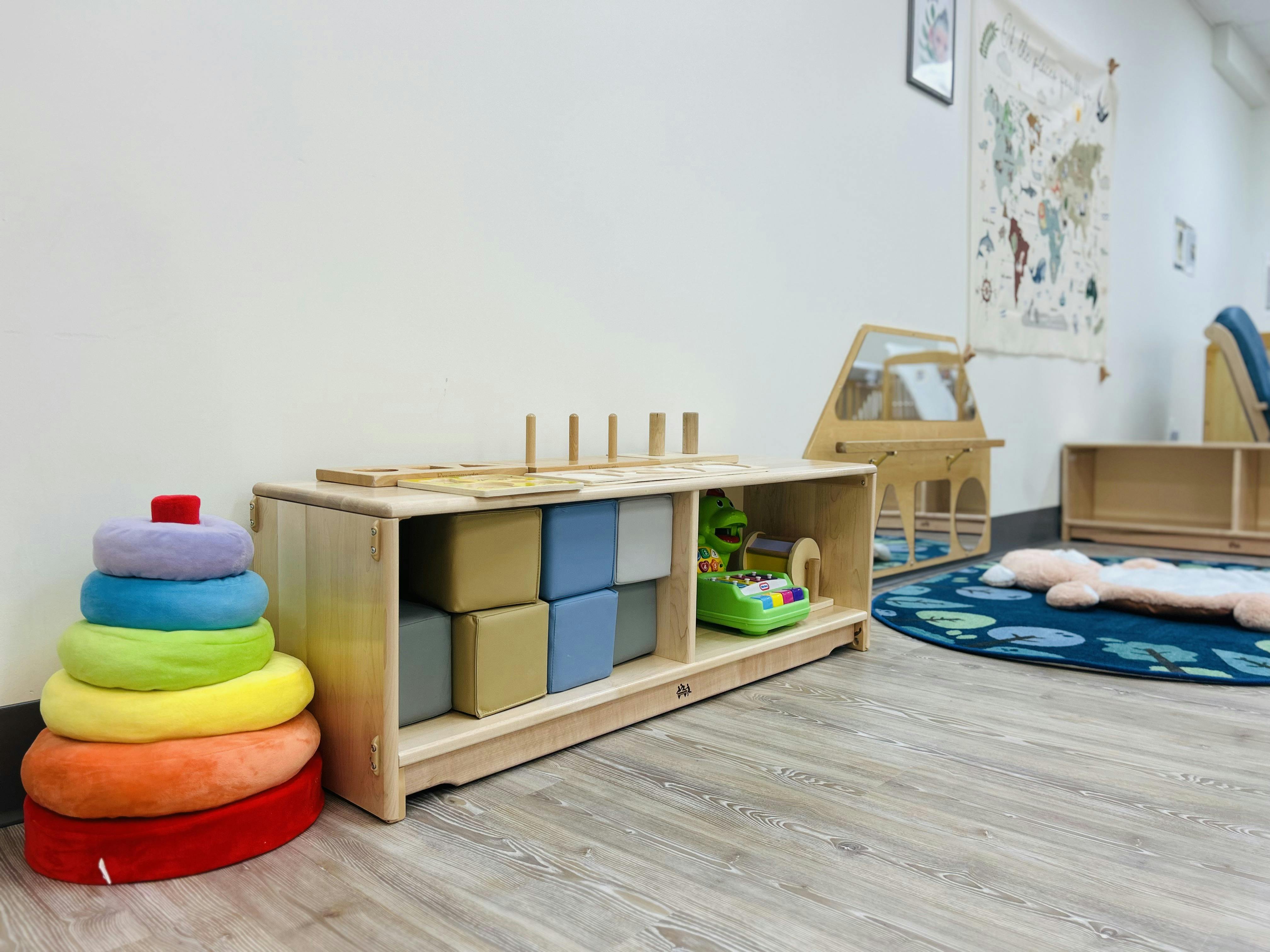 A playroom with a large rainbow stacking toy, a wooden shelf with play blocks