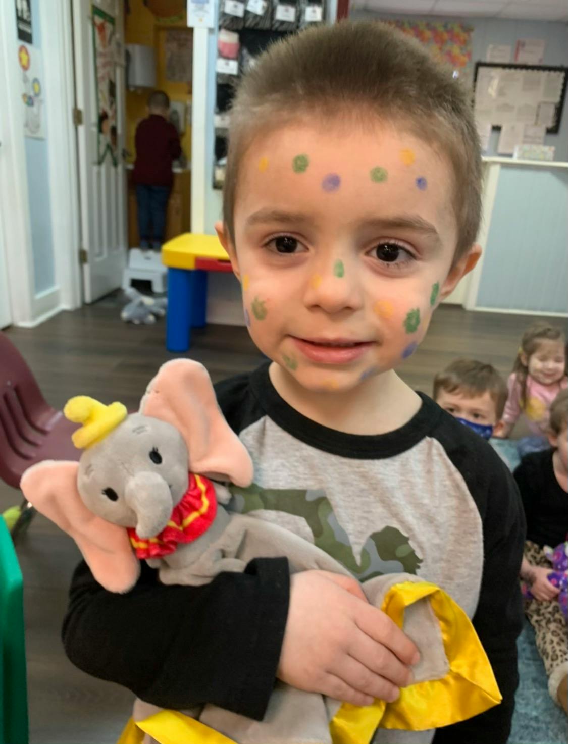 Child with face paint holding a Dumbo plush toy
