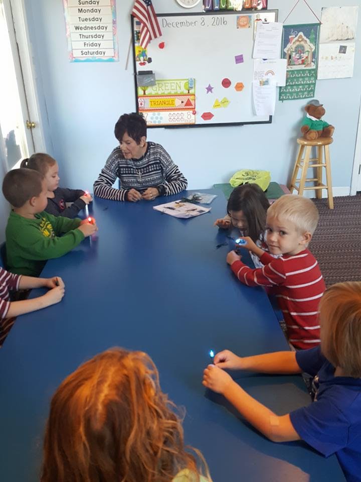Adult and children sitting around a table with small lights