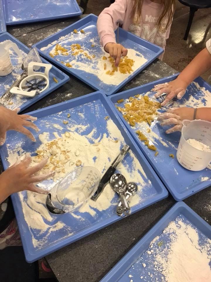 Multiple people's hands mixing flour and pasta on blue trays