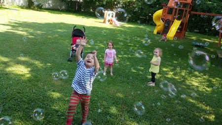 Child reaching for bubbles in a grassy yard with other children
