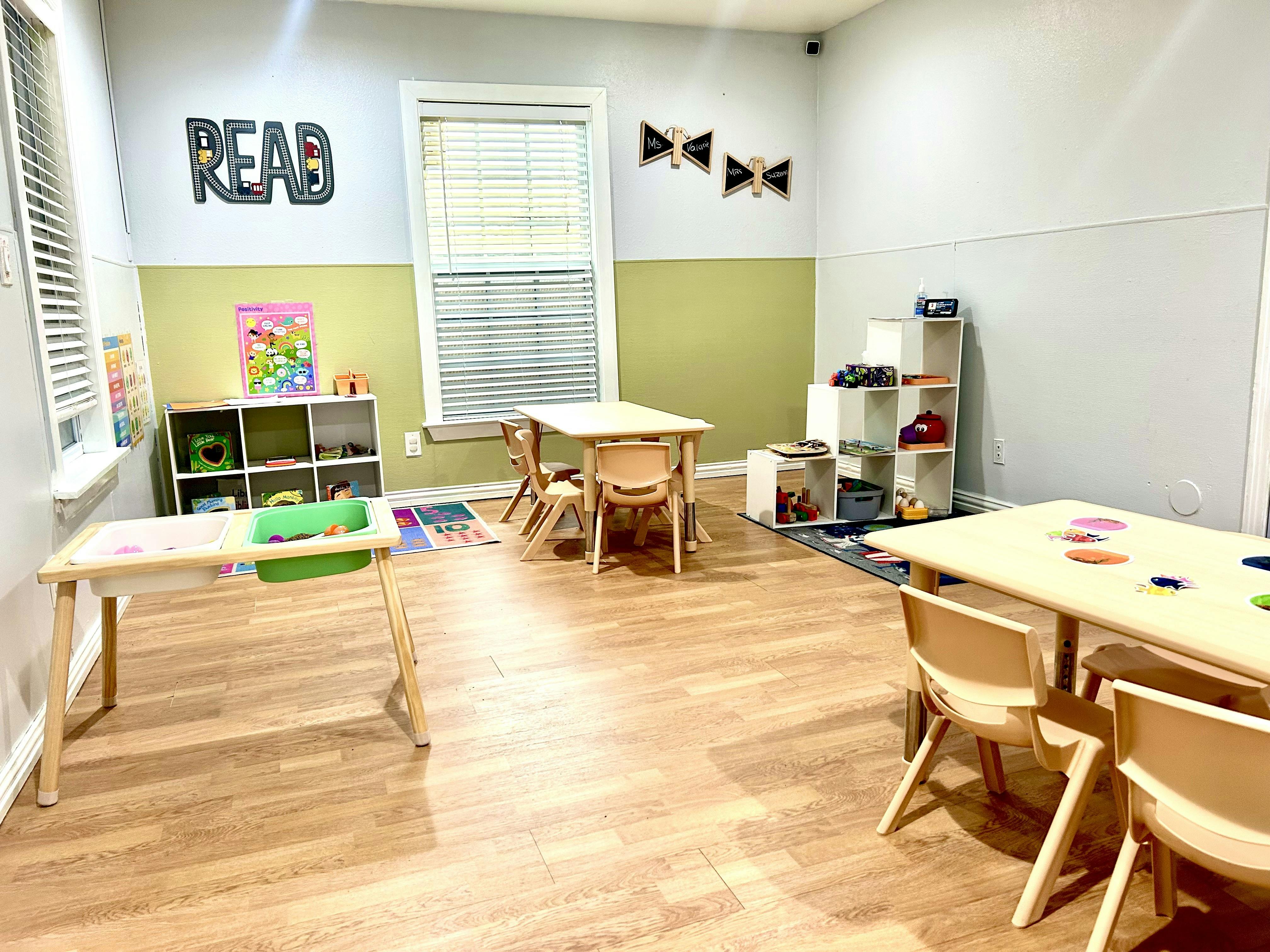 Classroom with small tables and chairs, shelves with toys, and a "READ" sign