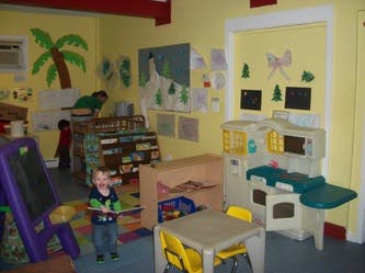 Child standing in a classroom with play kitchen and easel