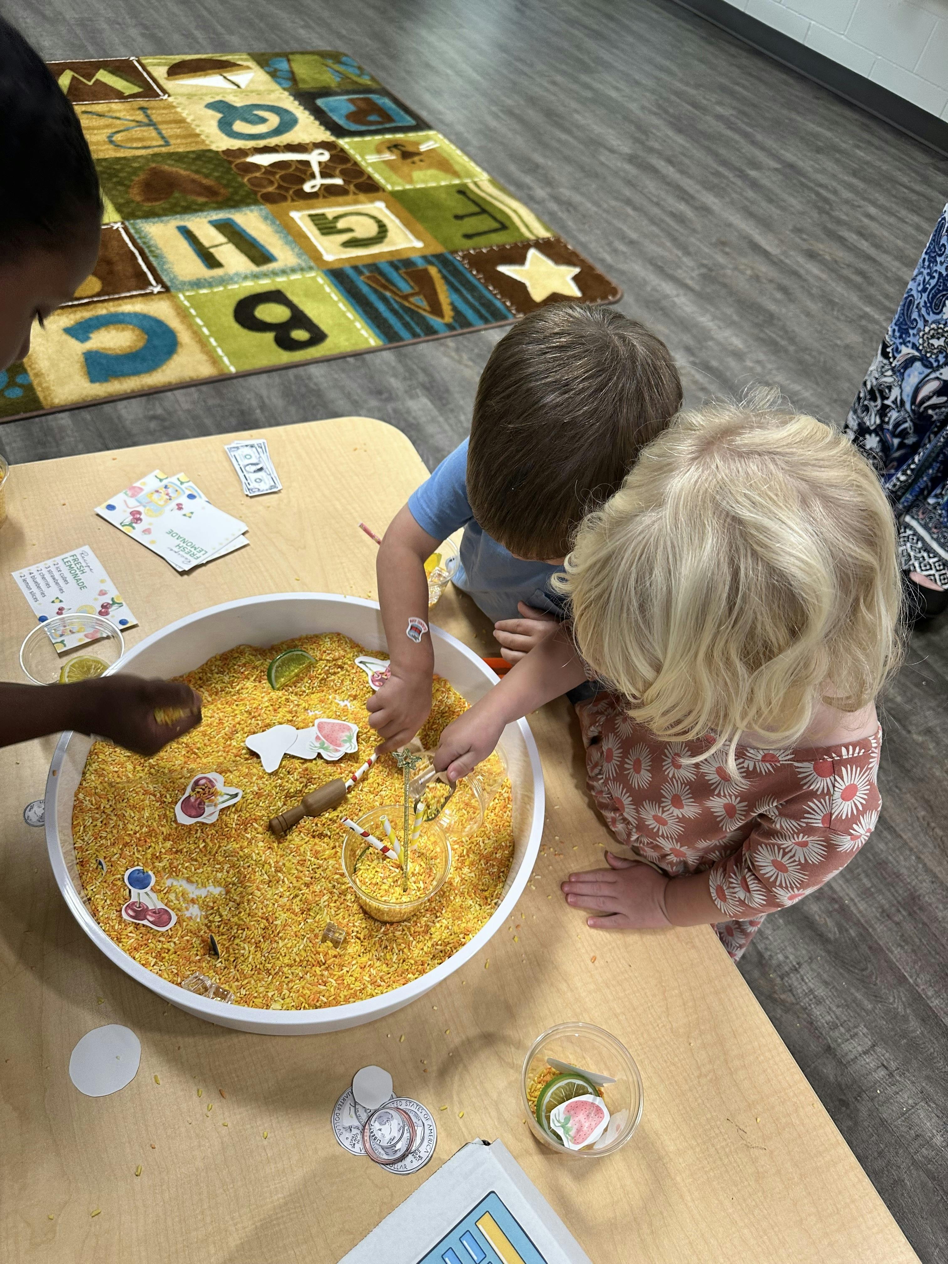 Three children playing with rice in a sensory bin