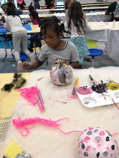 Child painting a pumpkin at a table with art supplies