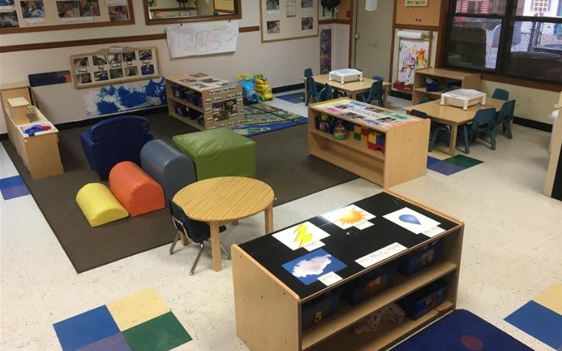 An empty classroom with small tables, chairs, and play equipment