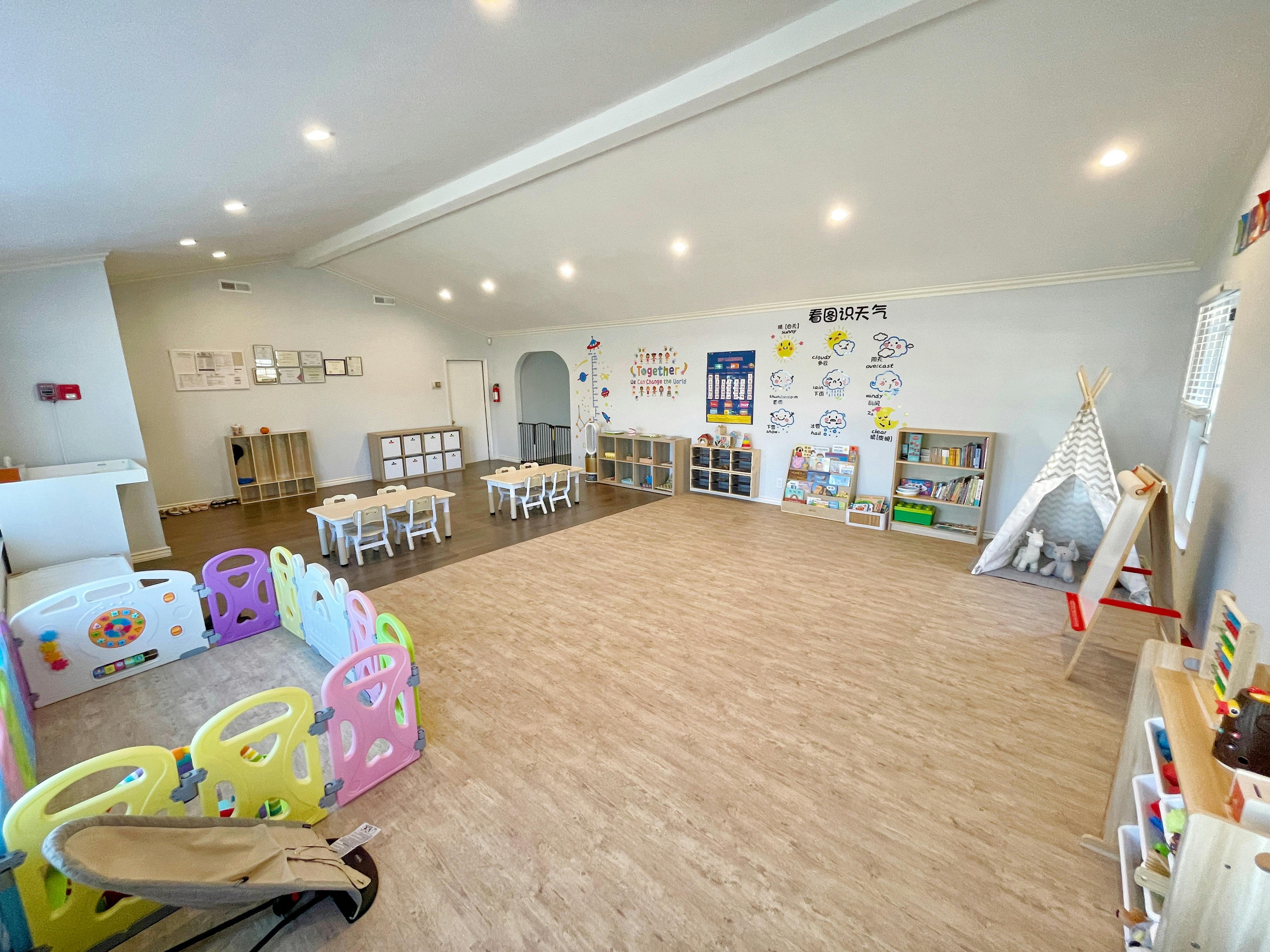 Empty classroom with small tables and chairs, playpen, and teepee