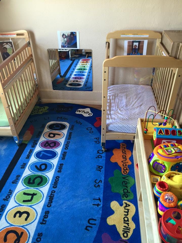 Two cribs in a room with a blue rug with numbers and letters