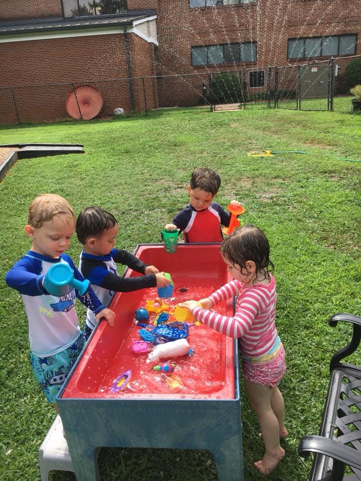 Children playing with water and toys in a water table outdoors