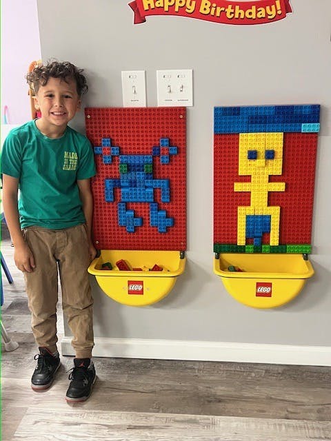 Smiling child standing next to two red Lego base plates with attached figures