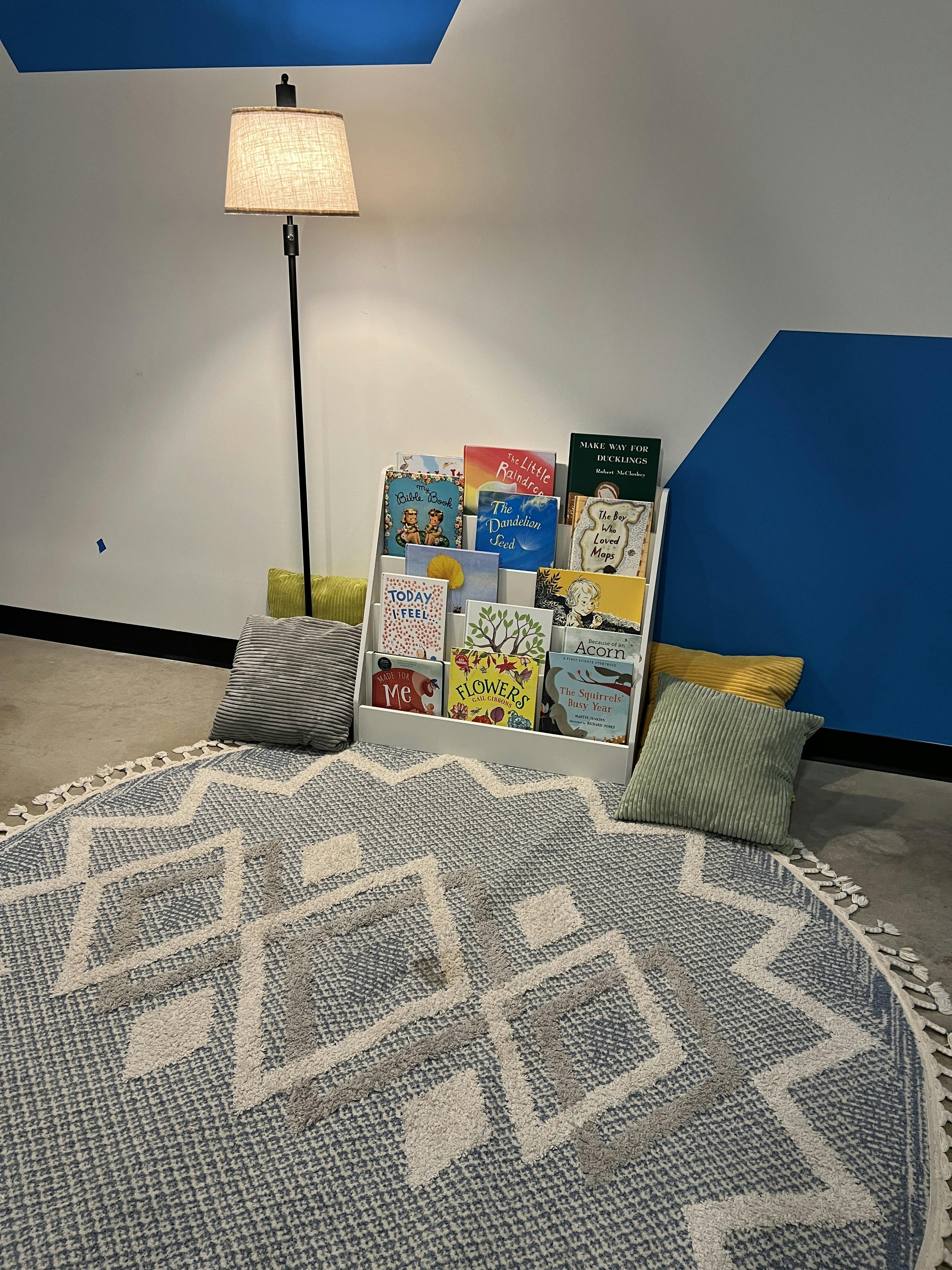 Childrens book display on a rug with a floor lamp and cushions