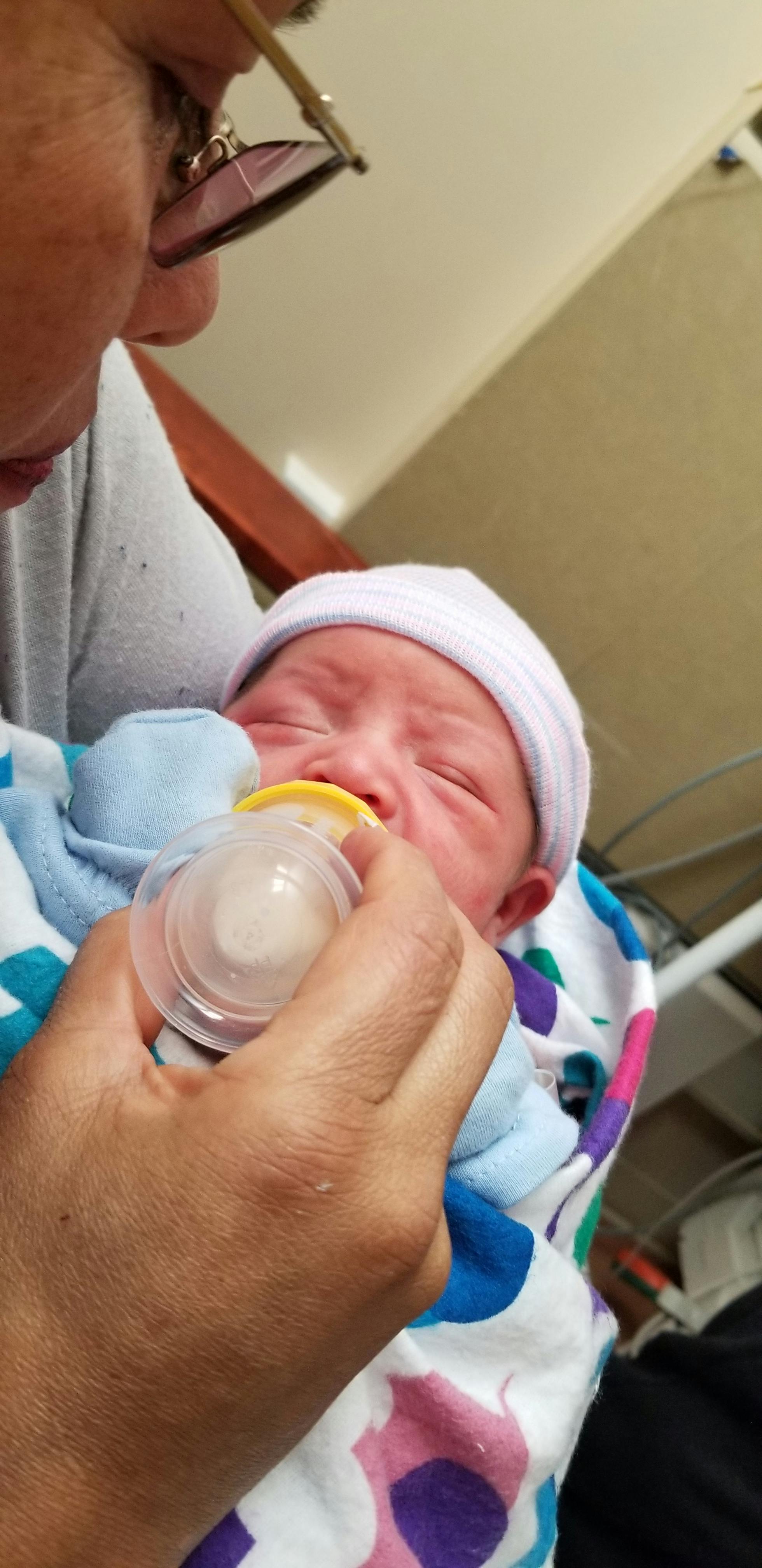 Person holding a baby wrapped in a blanket and feeding it with a bottle
