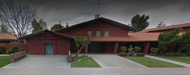 Red building with a cross on the roof and a driveway leading to the entrance