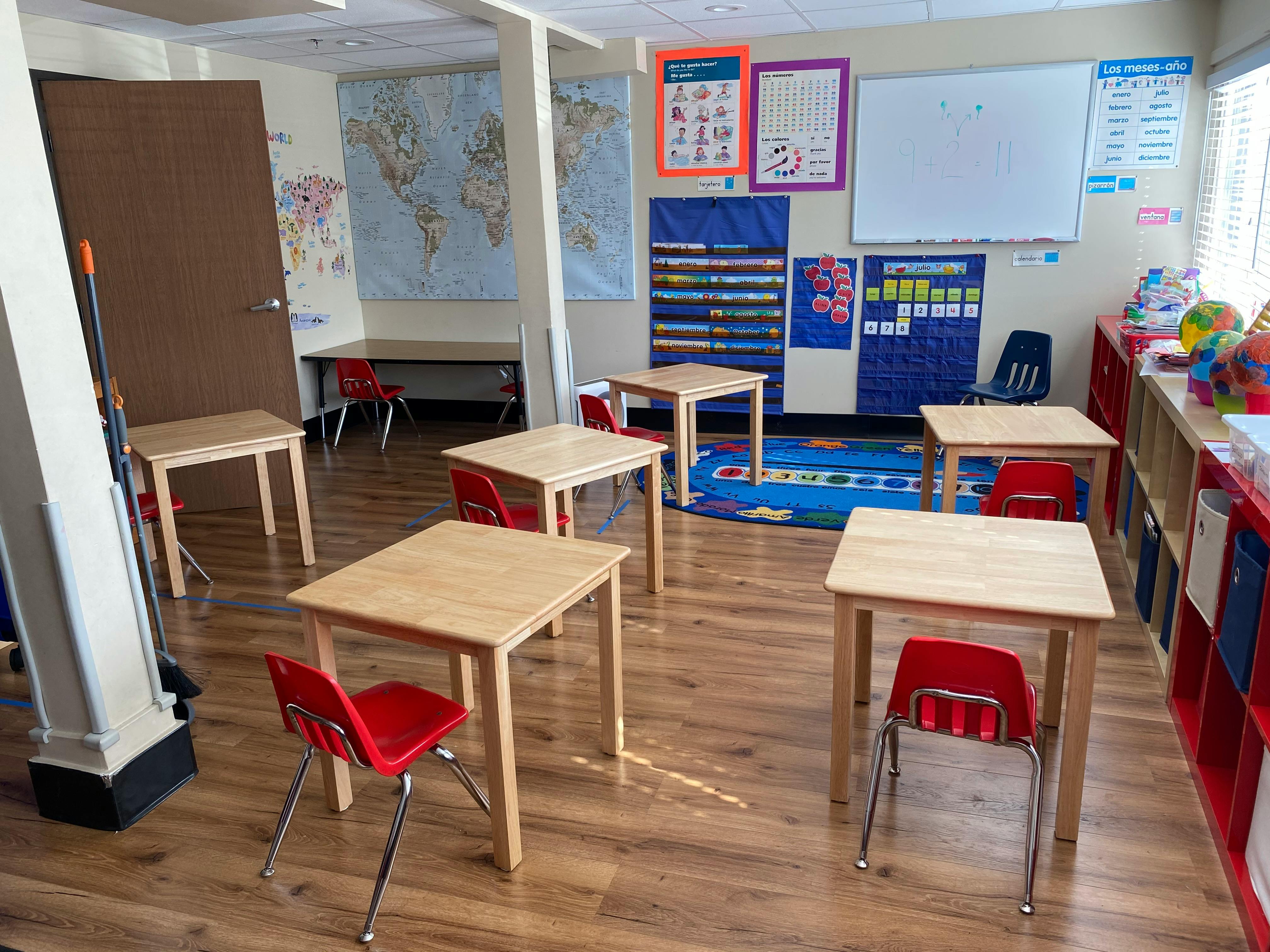 Empty classroom with small wooden tables and red chairs