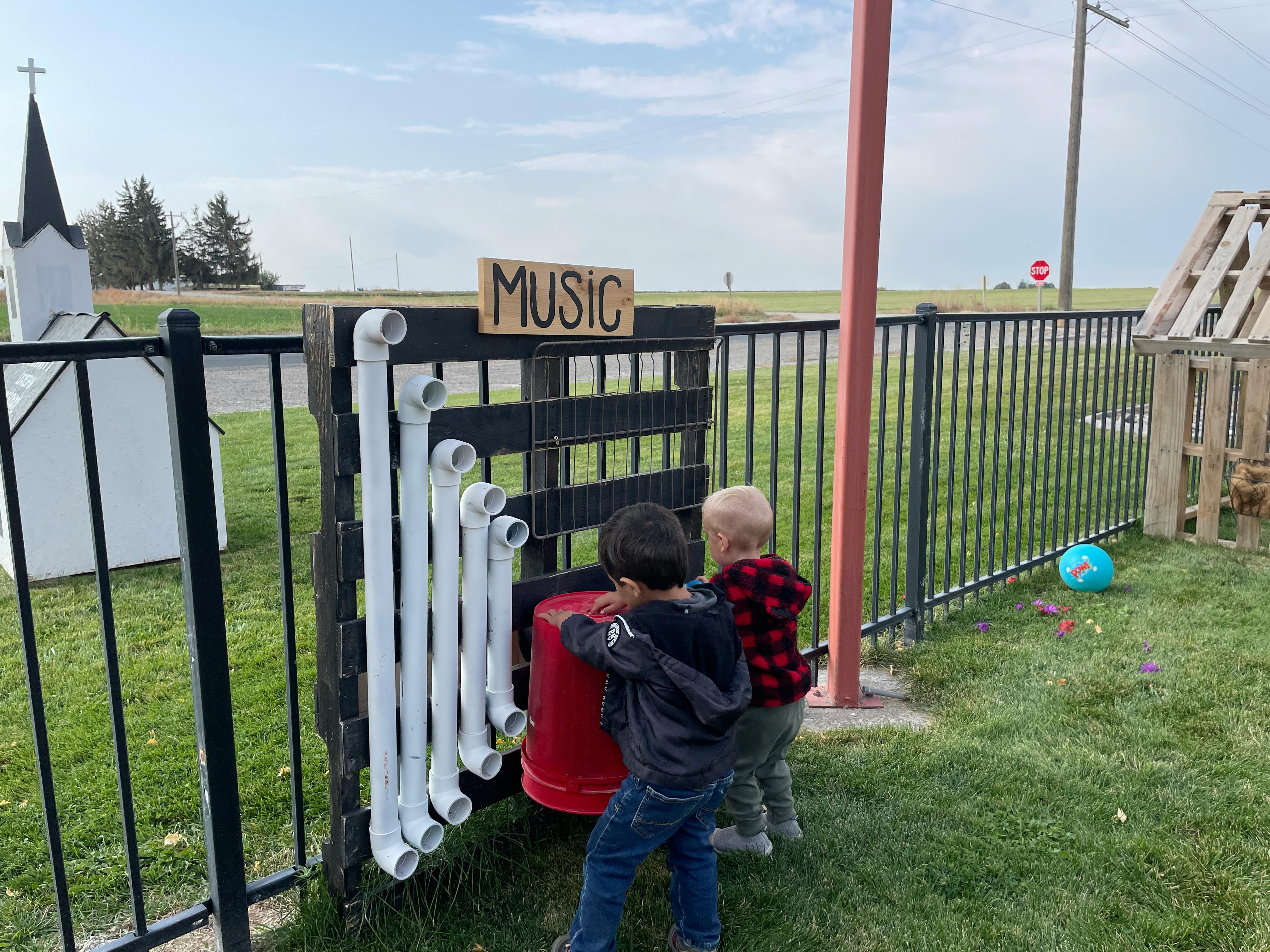 Two children playing with a music wall made of pipes