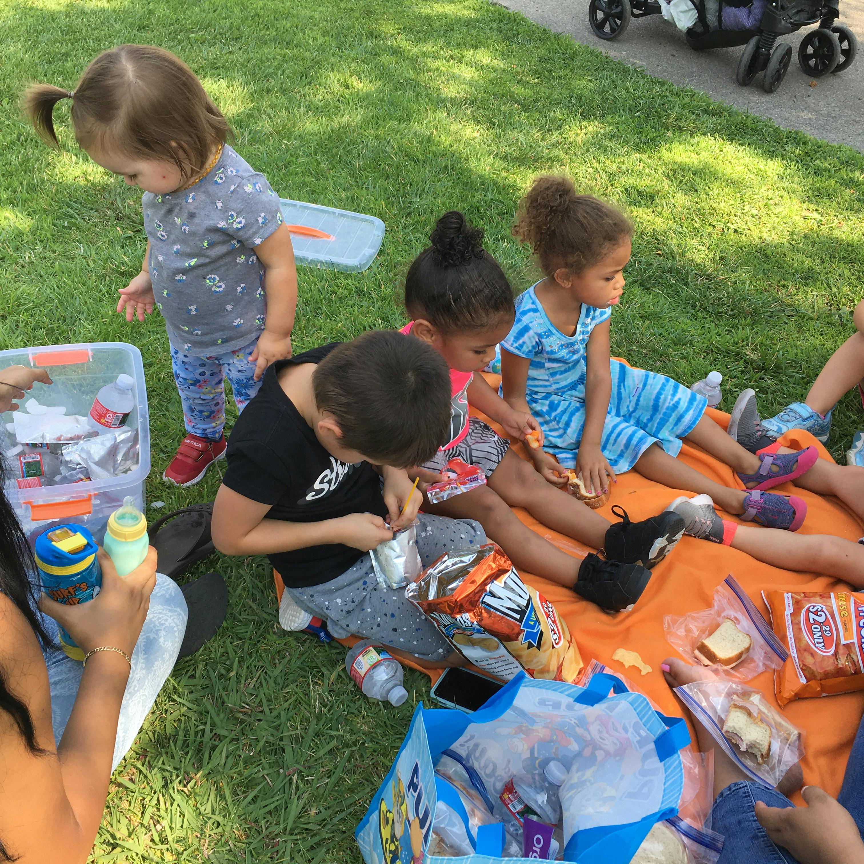 Children sitting on a blanket on grass, eating snacks