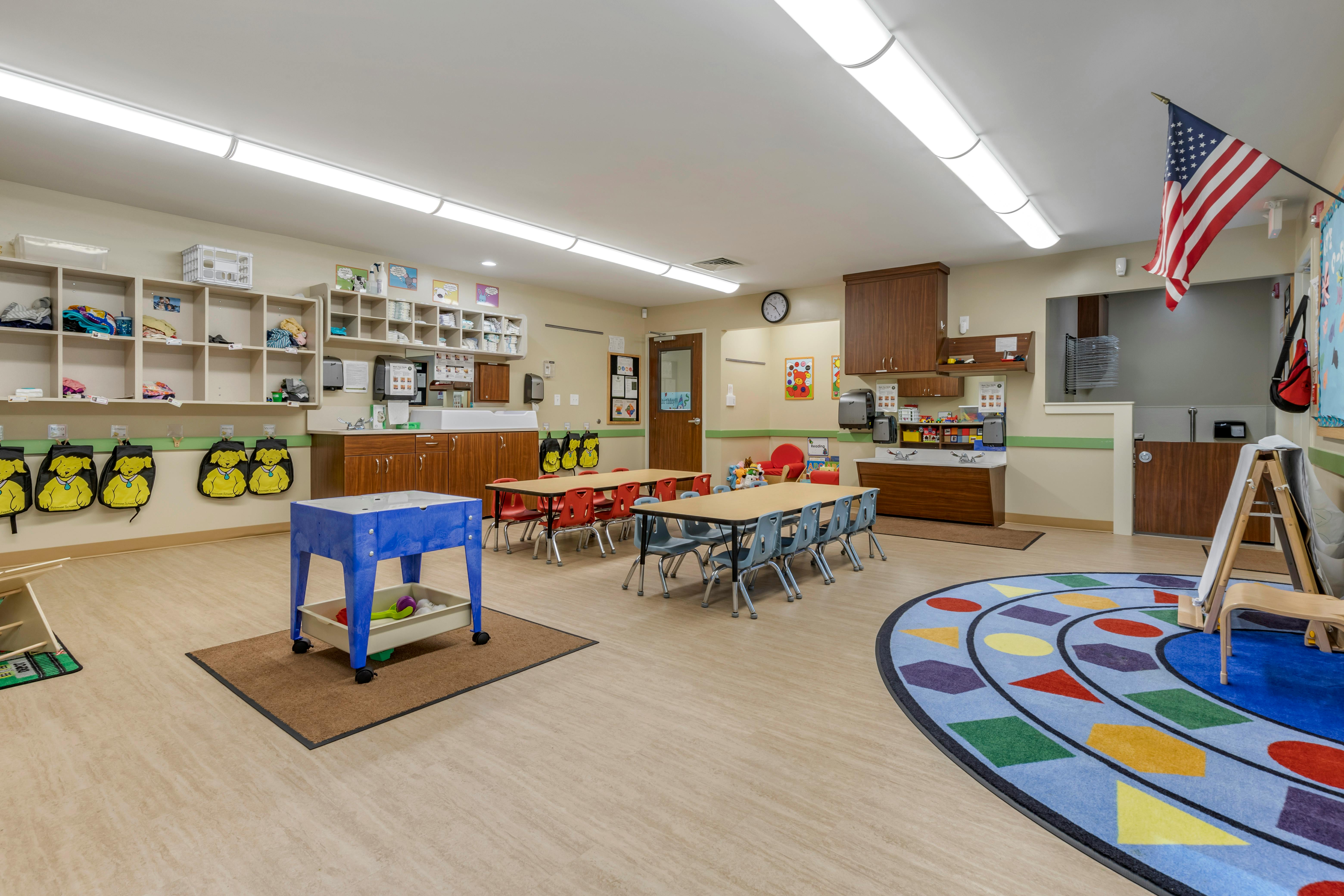 Classroom with child-sized tables and chairs, cubbies, changing station, and play rug