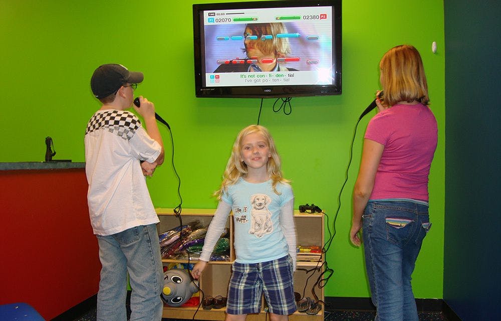 Three children singing karaoke in front of a television screen