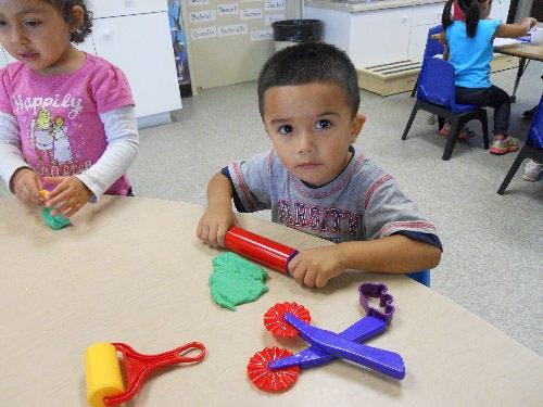 Child playing with modeling clay and tools at a table