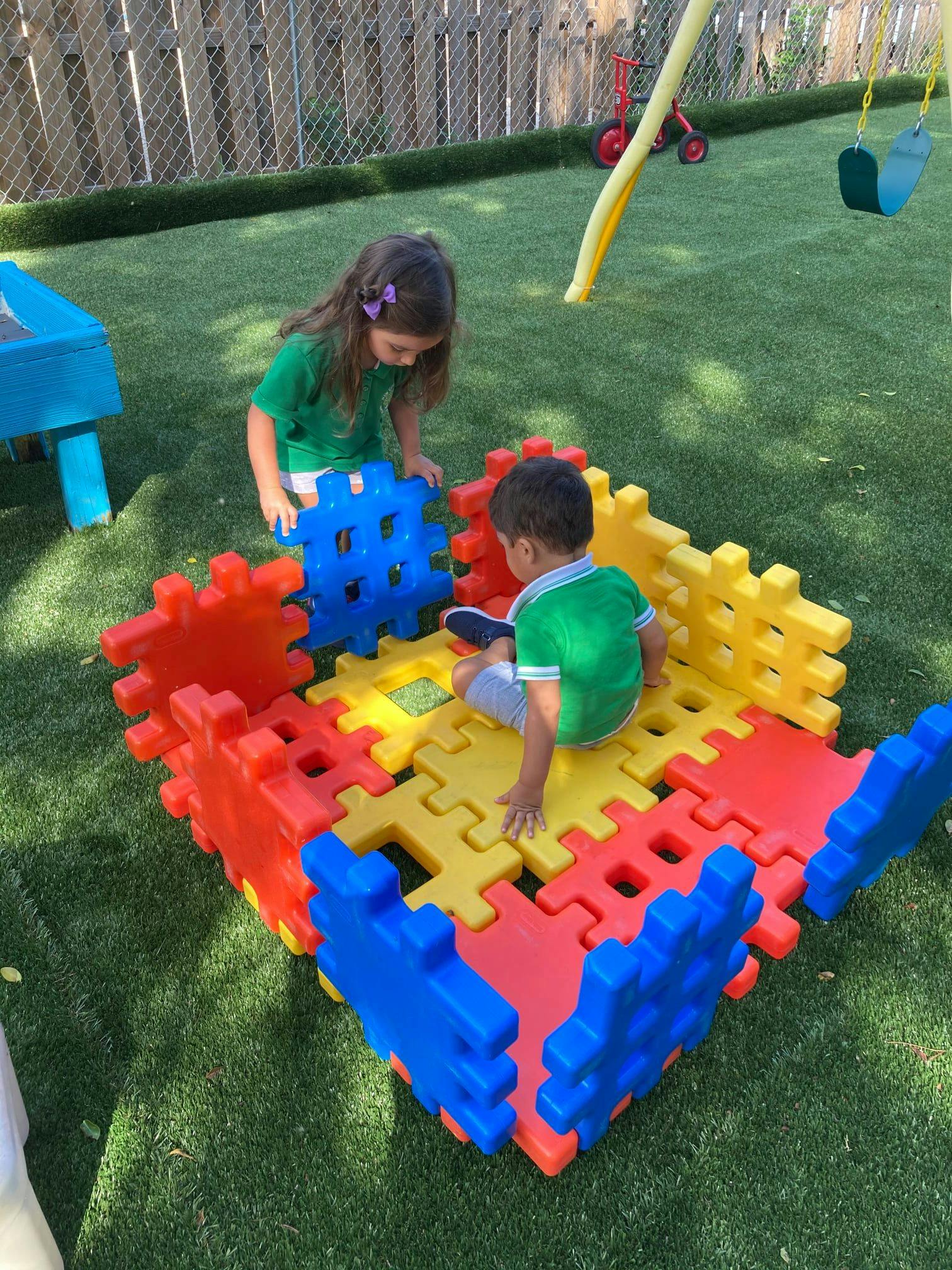 Two children playing with large colorful interlocking blocks on grass