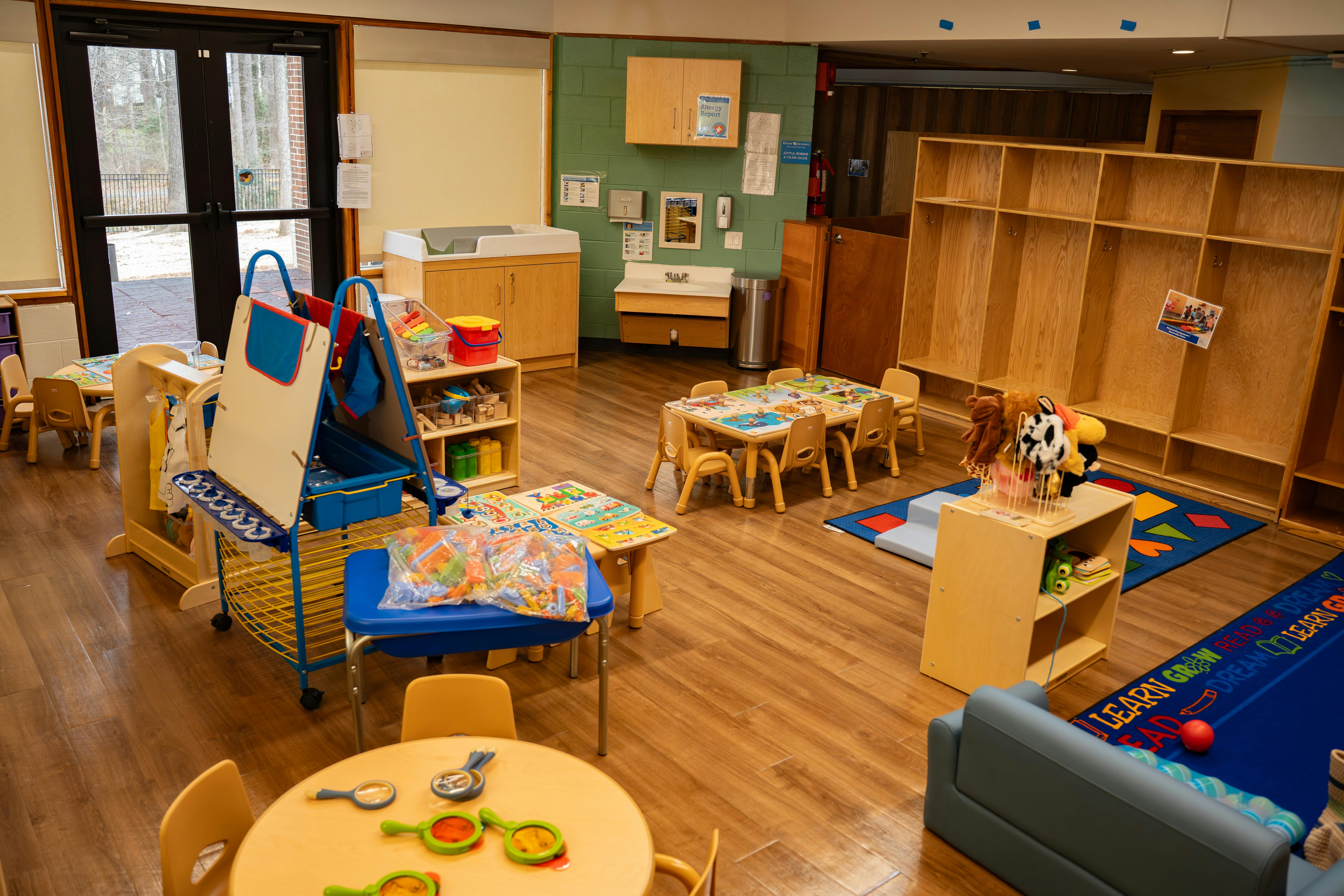 Classroom with small tables and chairs, cubbies, changing station, and play equipment