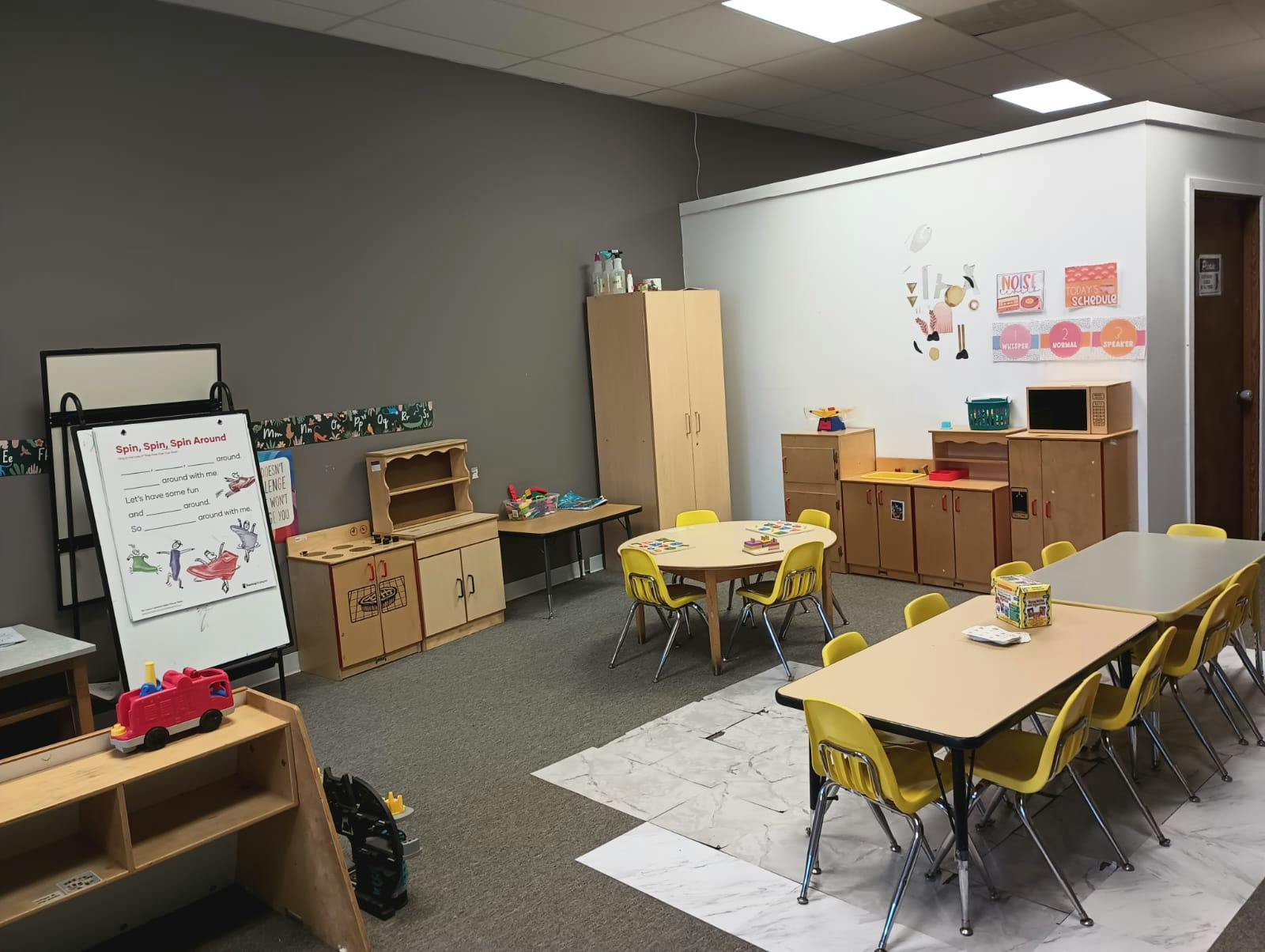 Classroom with small tables and chairs, storage cabinets, and a whiteboard