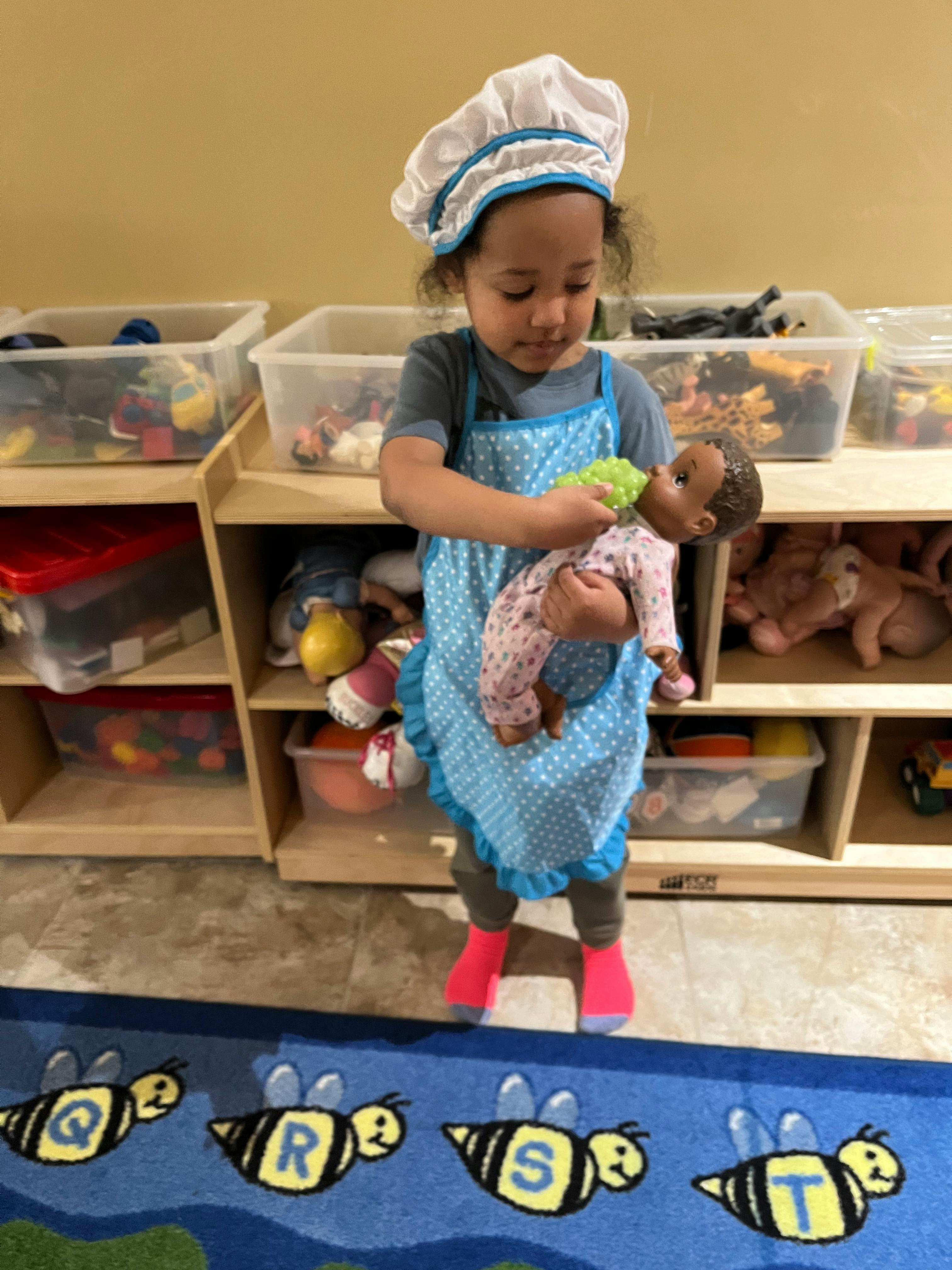 Child in chef hat and apron holding a doll
