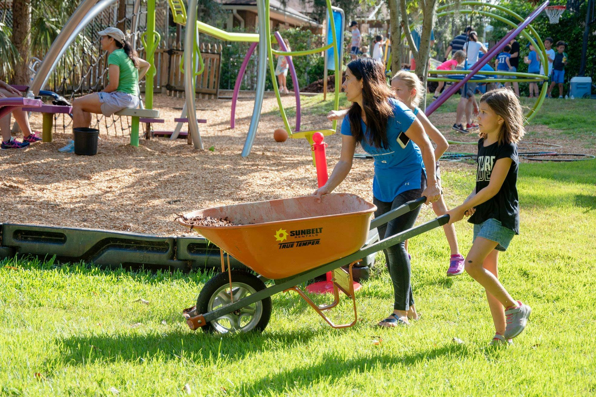 Person and child pushing a wheelbarrow filled with dirt