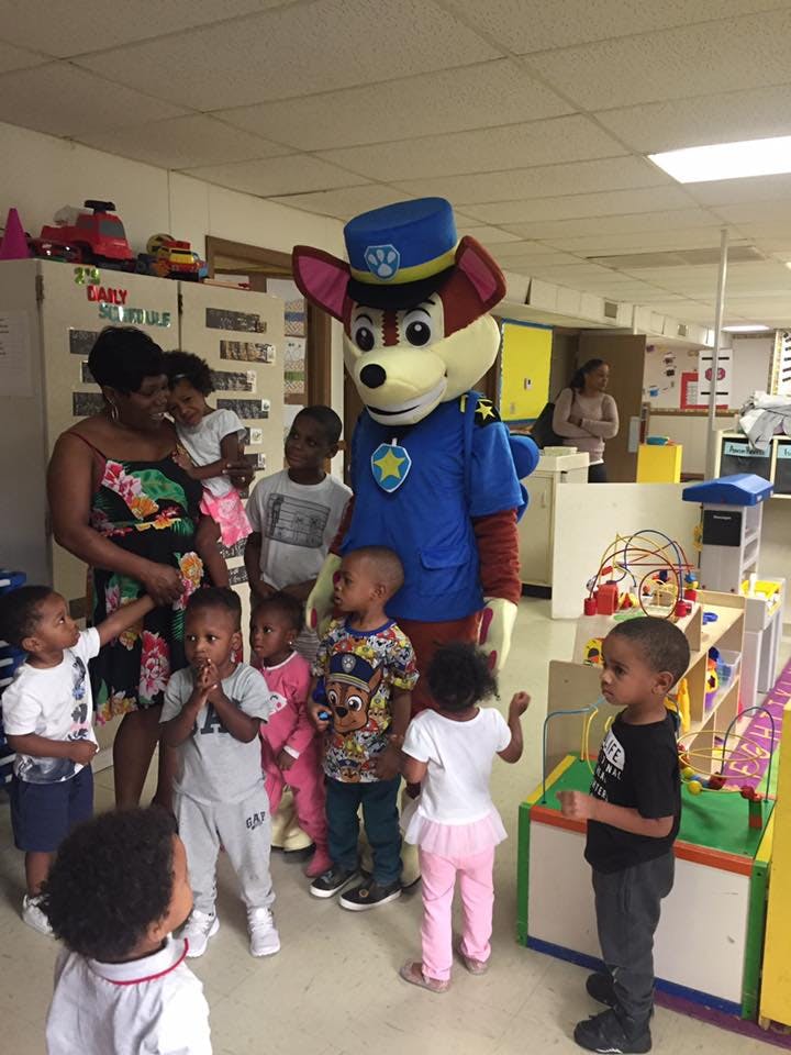 Person in a dog mascot costume with a group of children and an adult