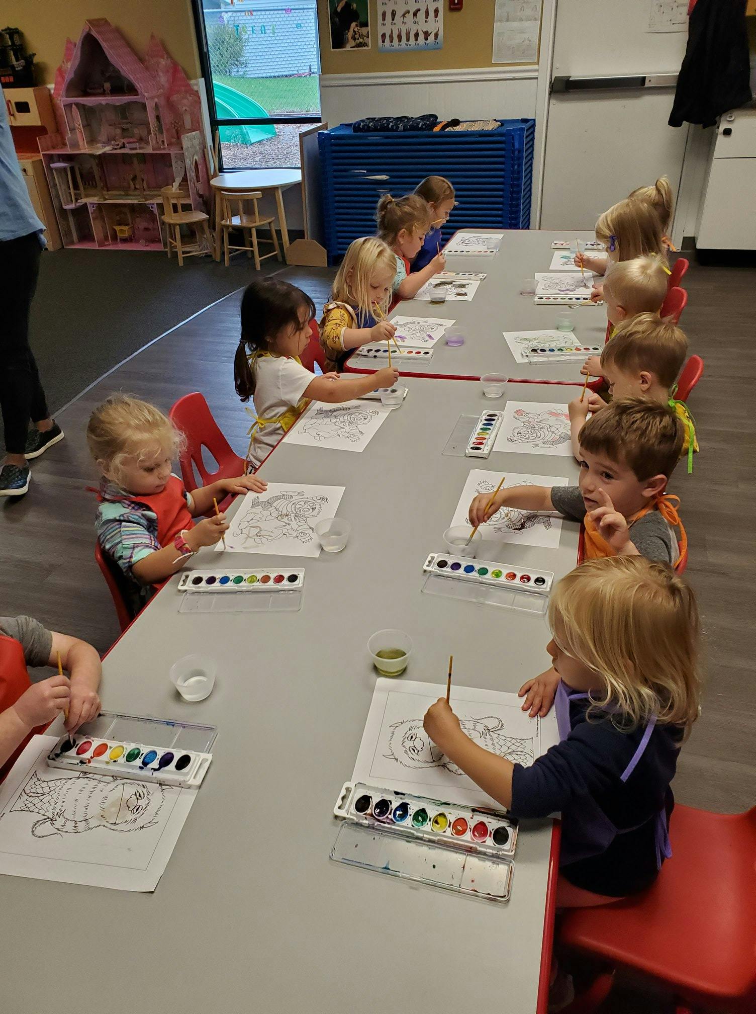 Children painting at a long table in a classroom
