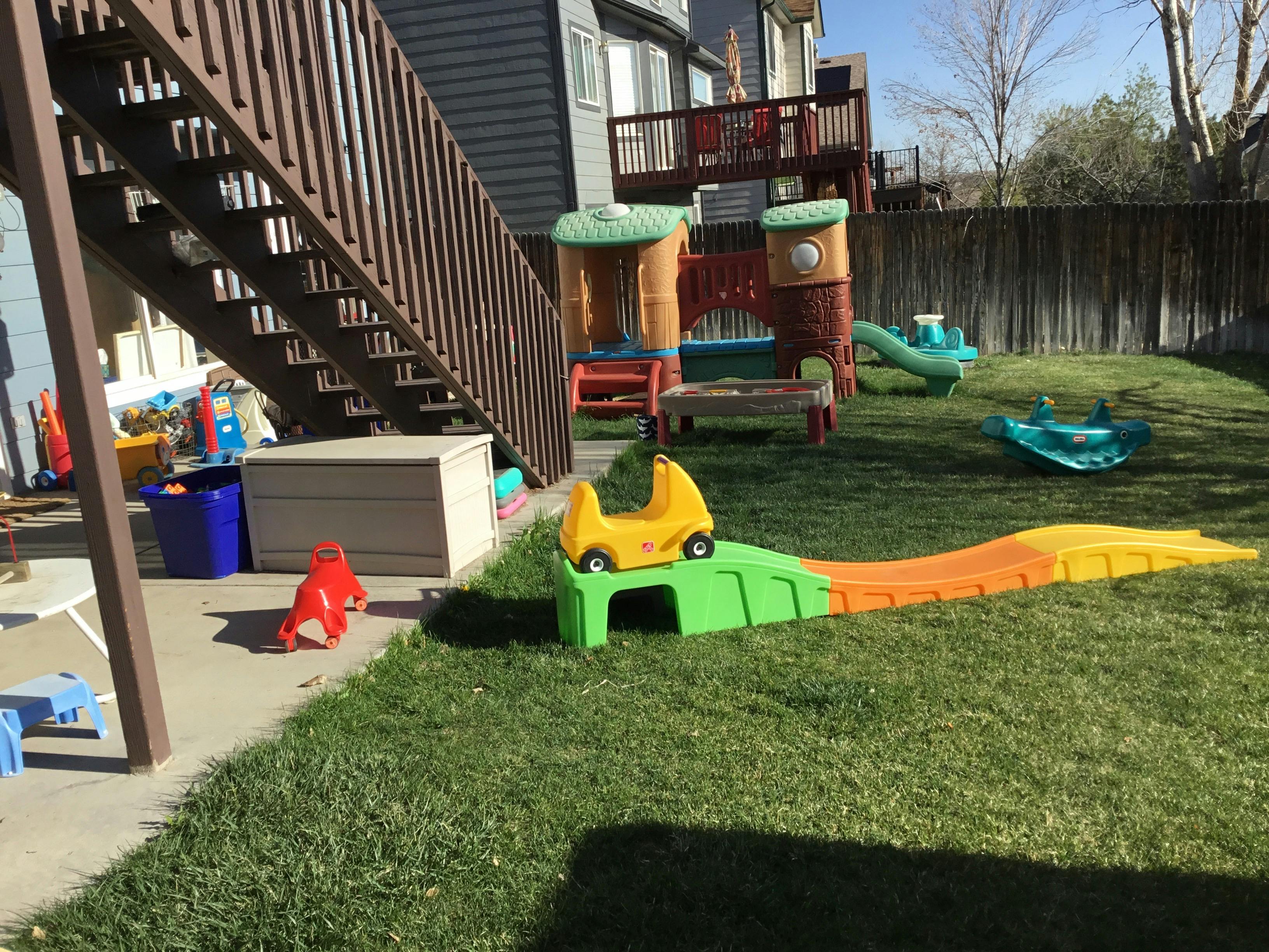 Backyard with a yellow toy car on a green and orange ramp