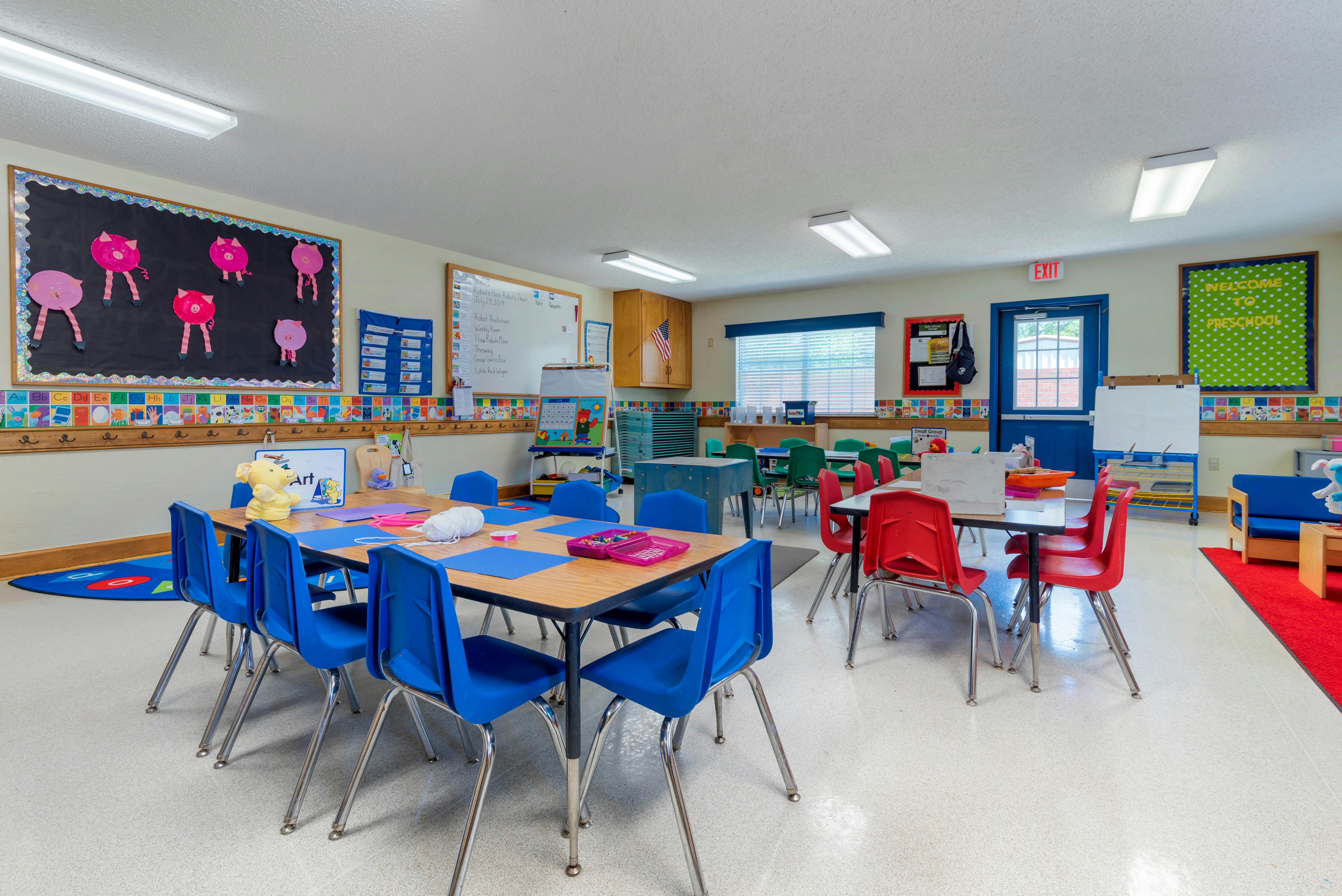 Classroom with child-sized tables and chairs, artwork on a bulletin board