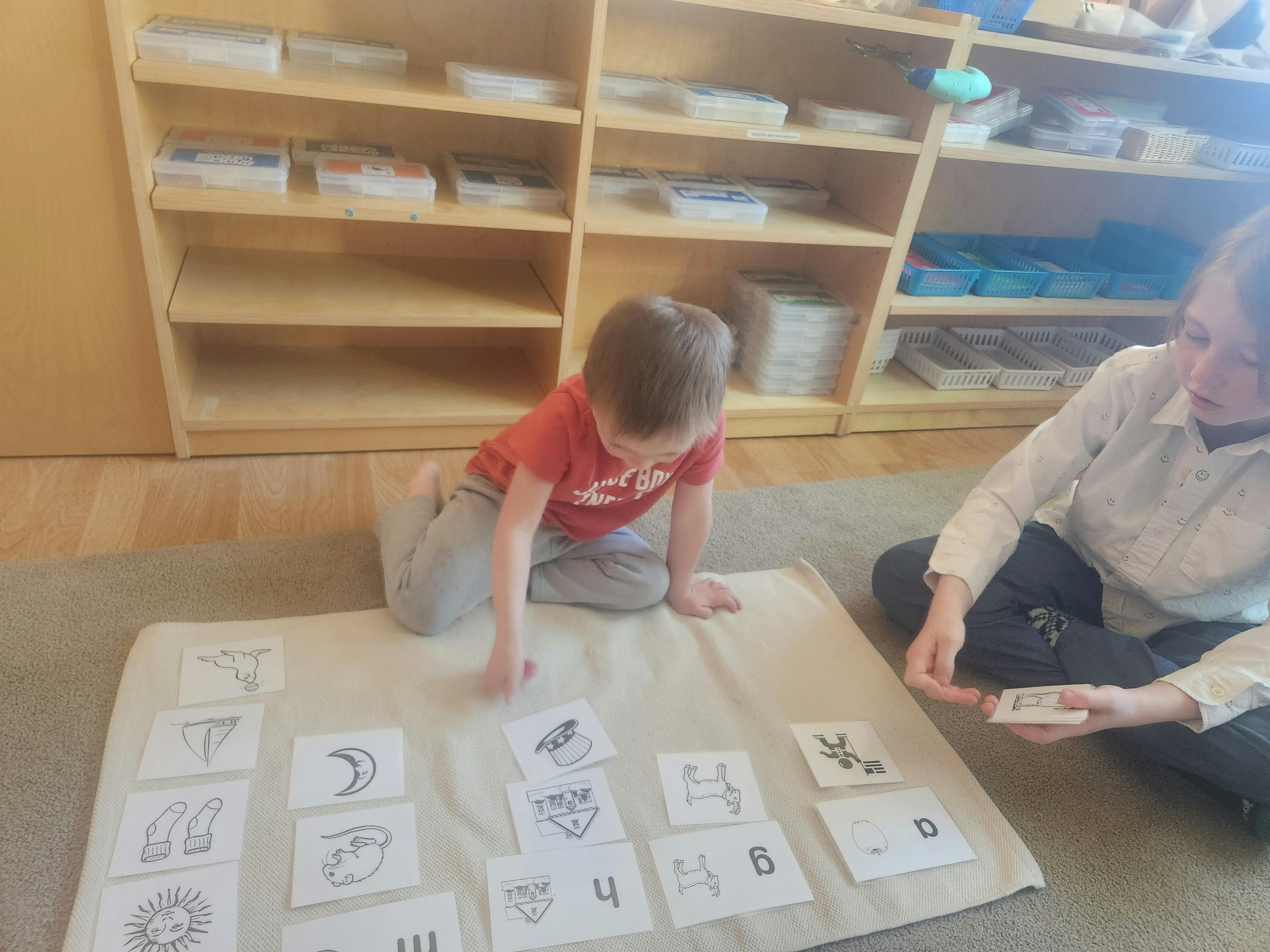 Child and person on floor with cards in a classroom, arranging cards with drawings