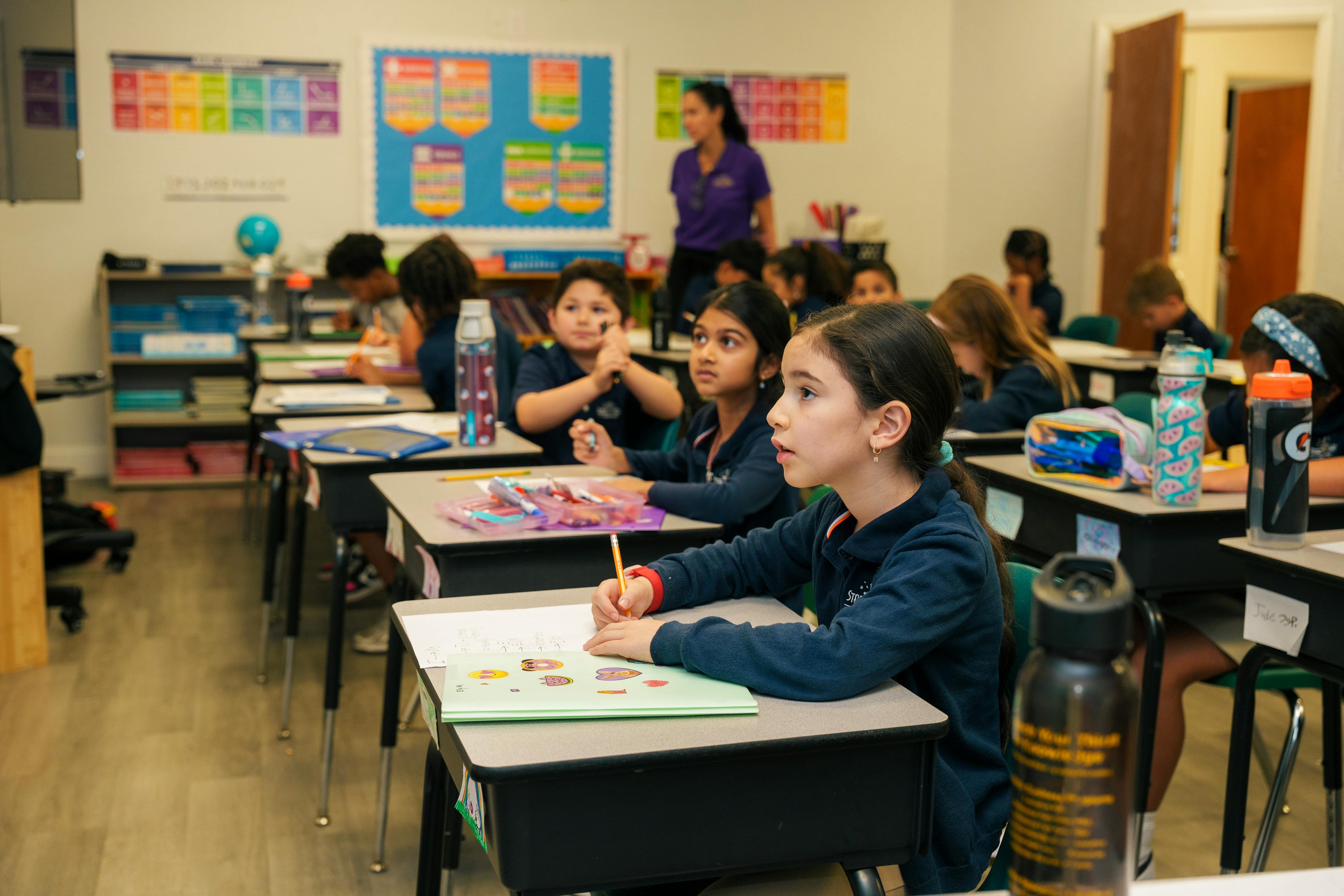 Children sitting at desks in a classroom, one child writing