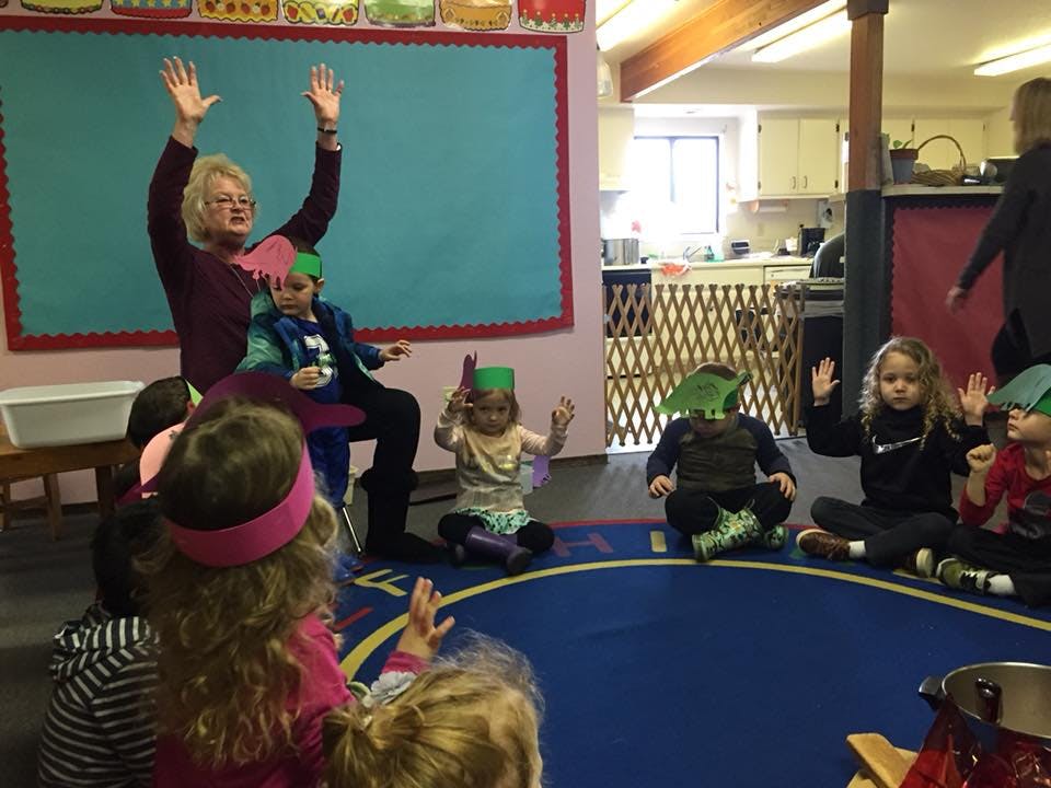 Adult and children raising hands in a classroom
