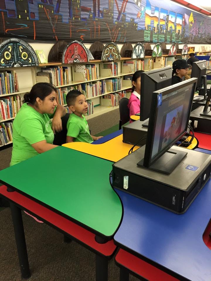 Adult and child sitting at colorful desks in front of computers