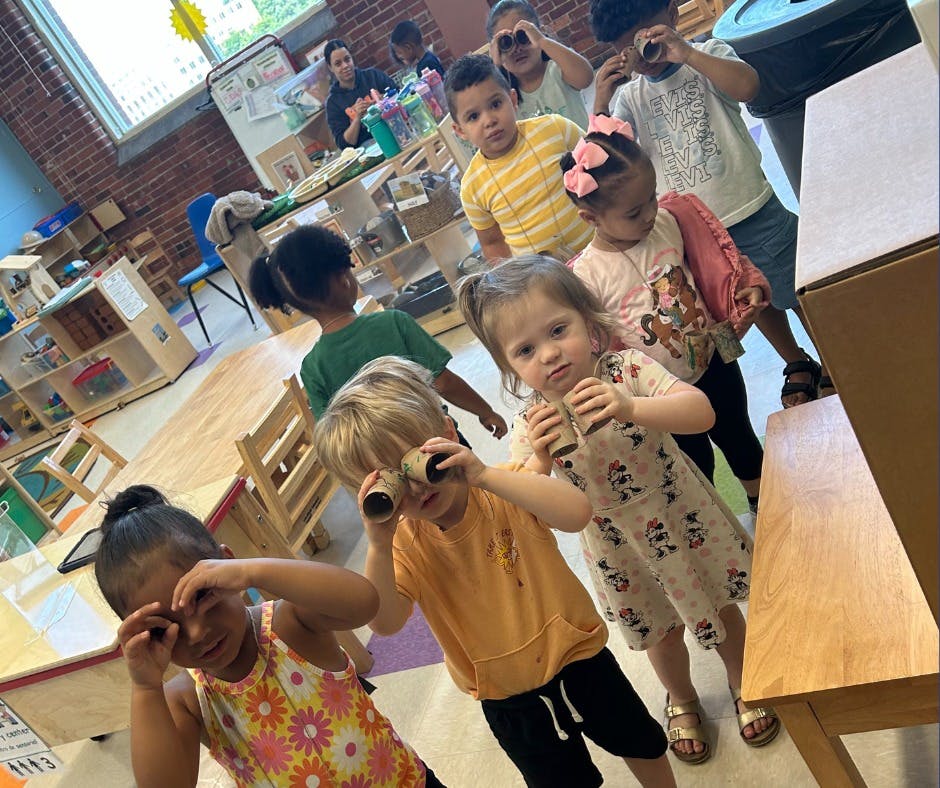 Children in a classroom looking through cardboard tubes like binoculars