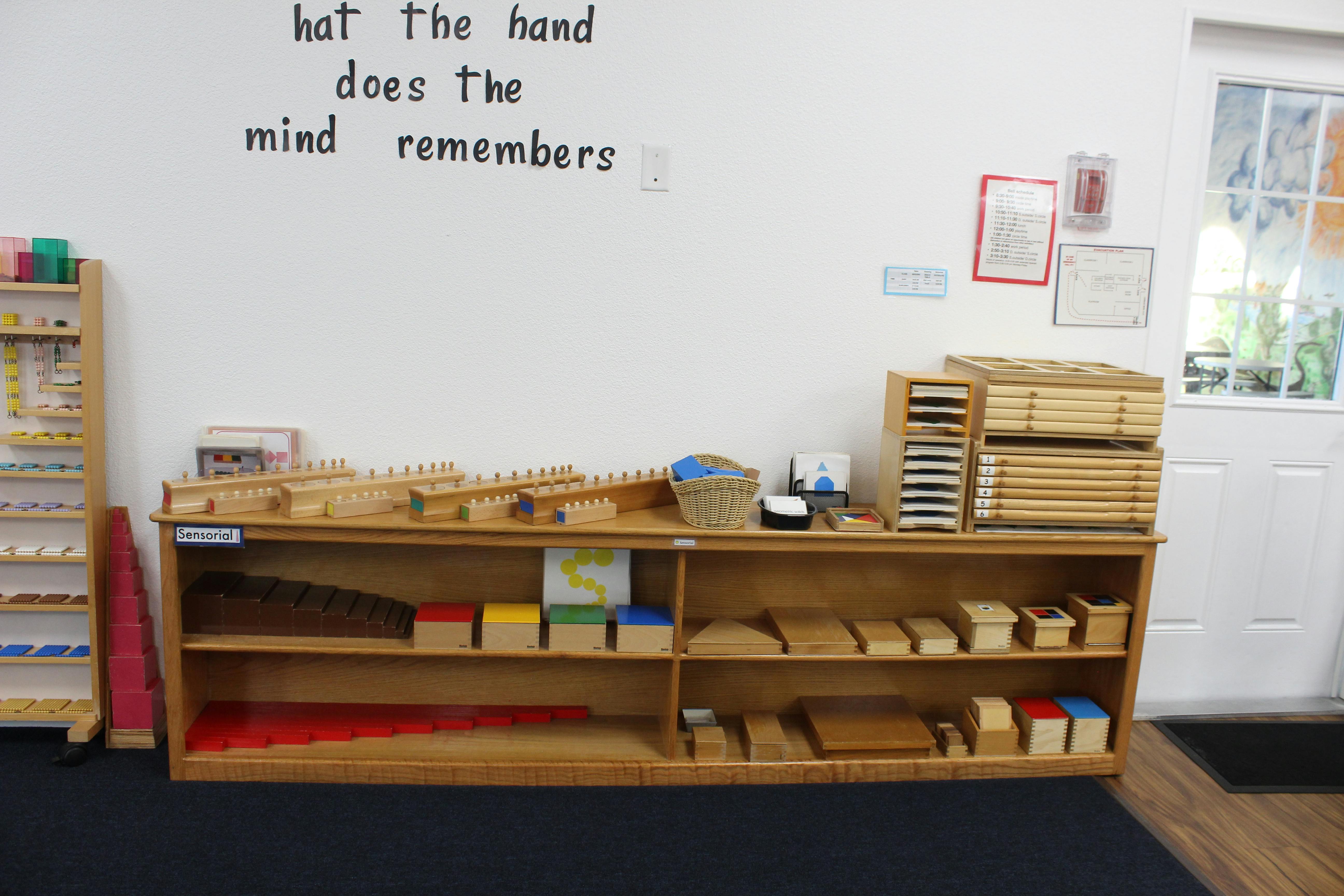 Classroom with Montessori materials on shelves and text on the wall
