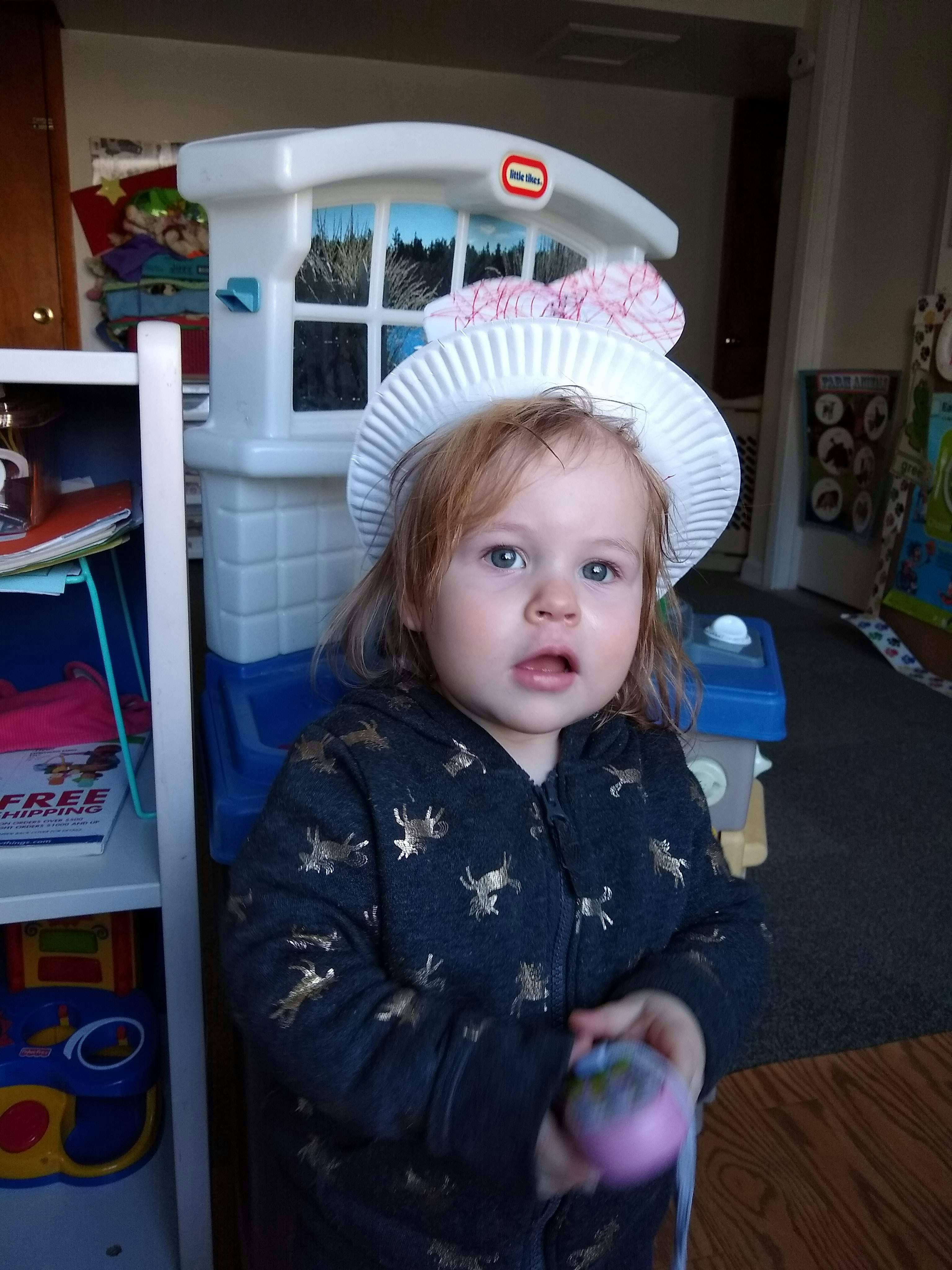 Child wearing a paper plate hat and holding a toy