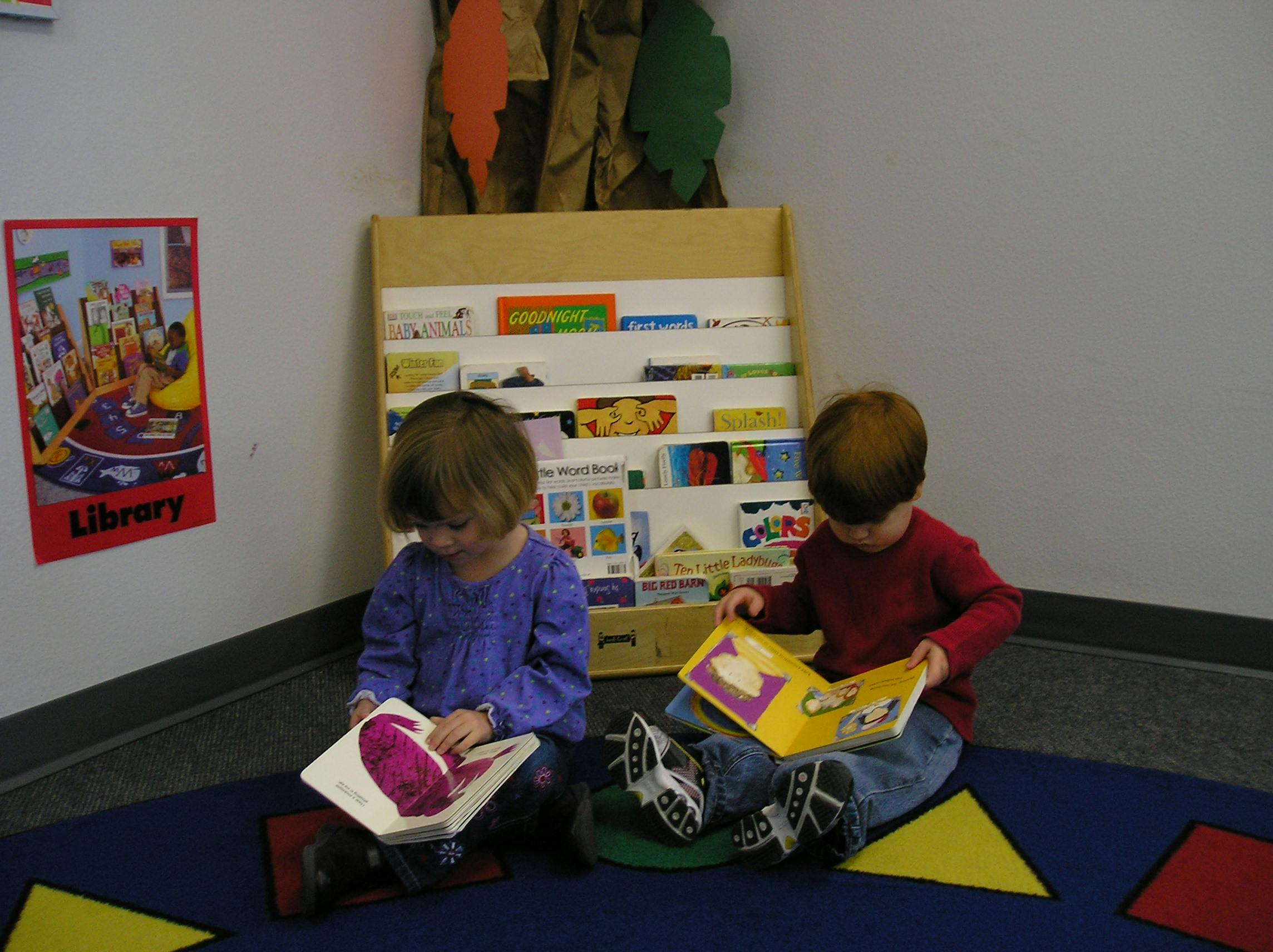 Two children sitting on the floor reading books in a classroom