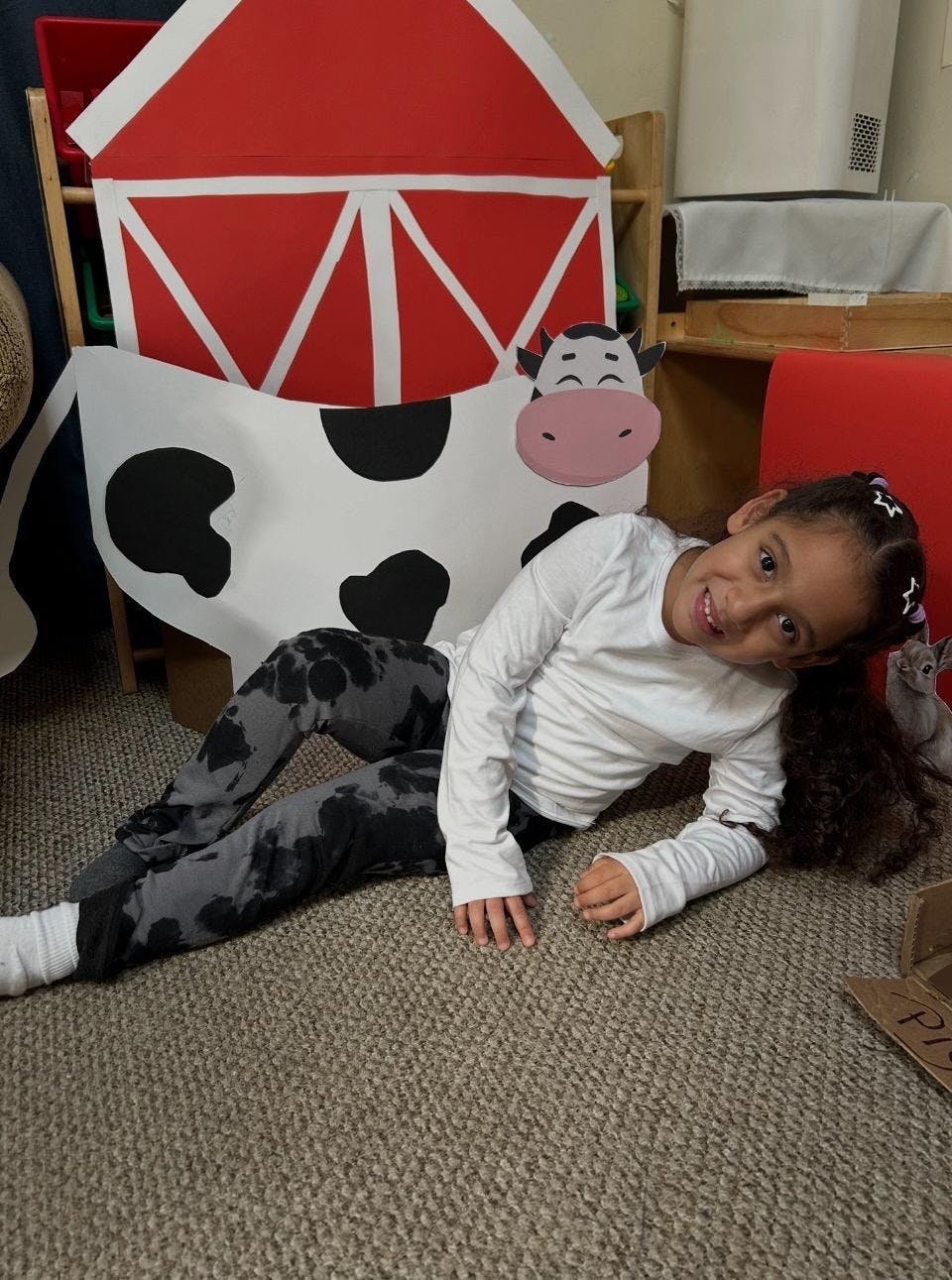 Child lying on the floor in front of cardboard cow and barn props